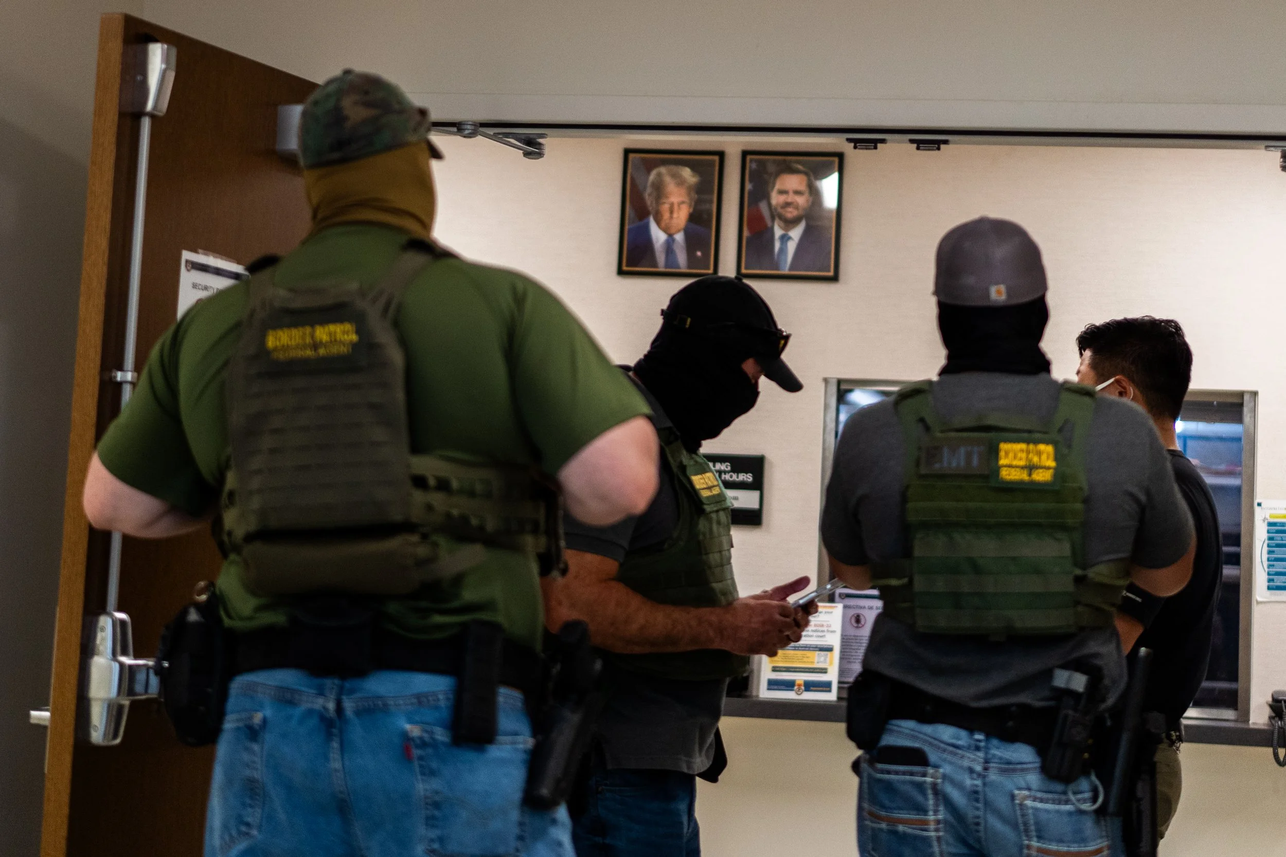 Masked agents stand beneath portraits of President Donald Trump and Vice President JD Vance as they wait for the immigration hearing to get out.
