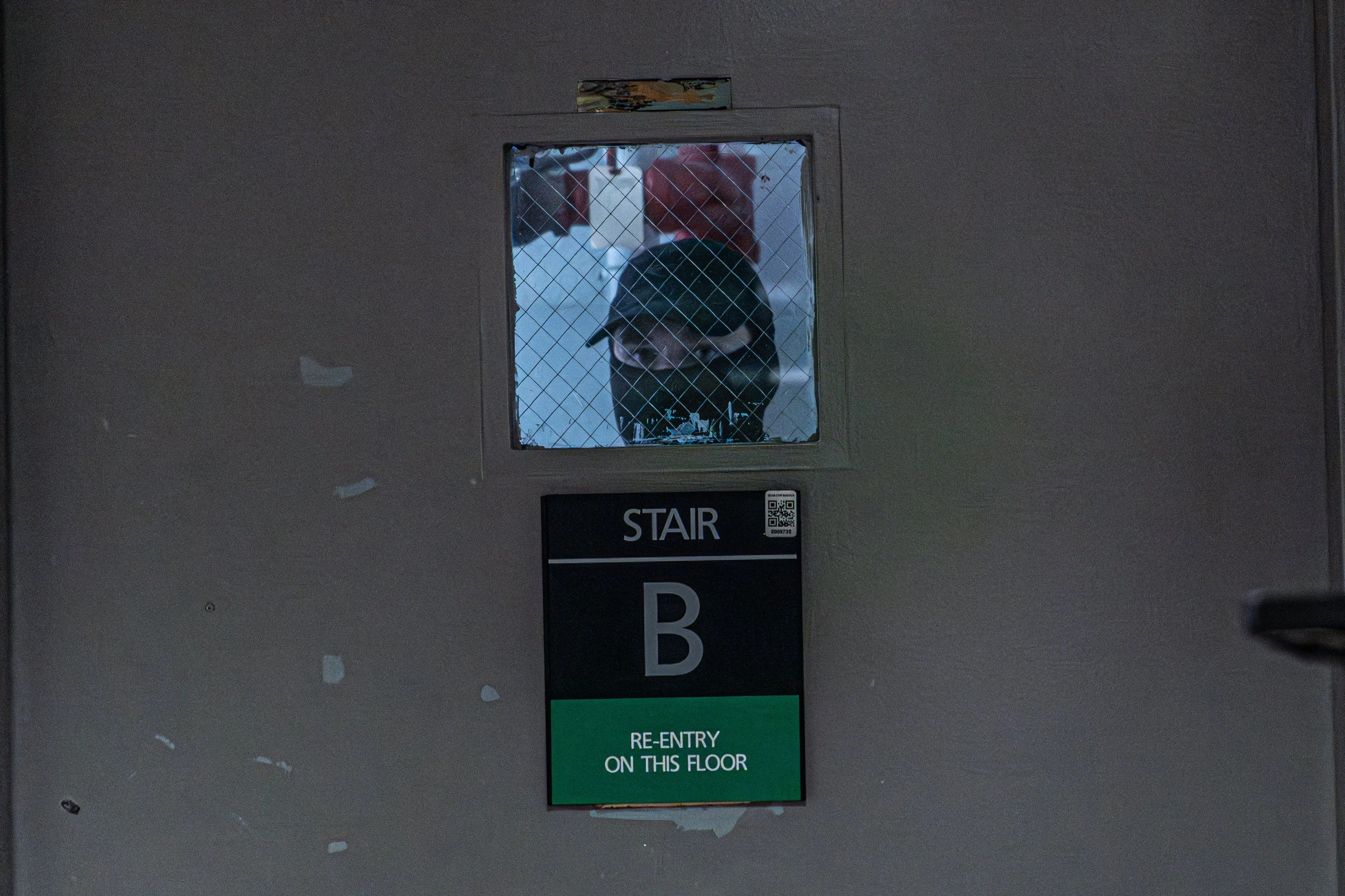 An ICE agent watches through the small window of the stairwell door after escorting a detained person inside. This stairwell leads to the 10th floor — a restricted area where those arrested are held before being transported.