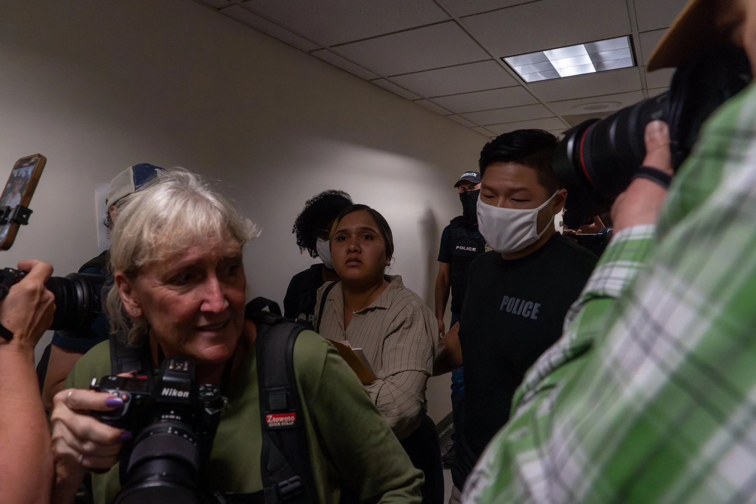 Shock washes over her face as she realizes the man beside her is an ICE agent. Moments earlier, she had walked out of her immigration hearing smiling. Now she is frozen, surrounded. After this photo was taken, she was led into a stairwell — her cries