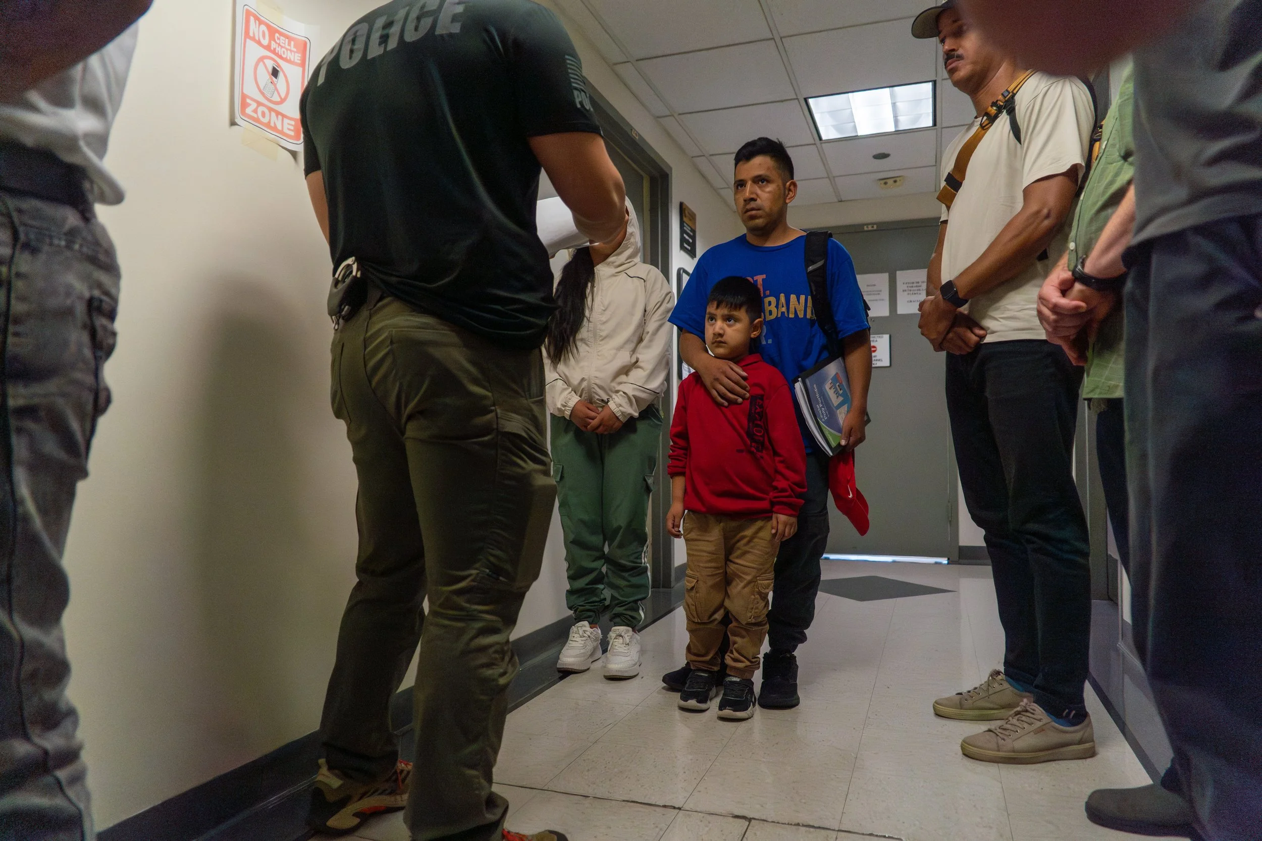 A father grips his son tightly as ICE checks if he is on their deportation list. Both of them are visibly frightened — frozen in place, waiting. After several tense minutes, they are allowed to leave. But the fear lingers.