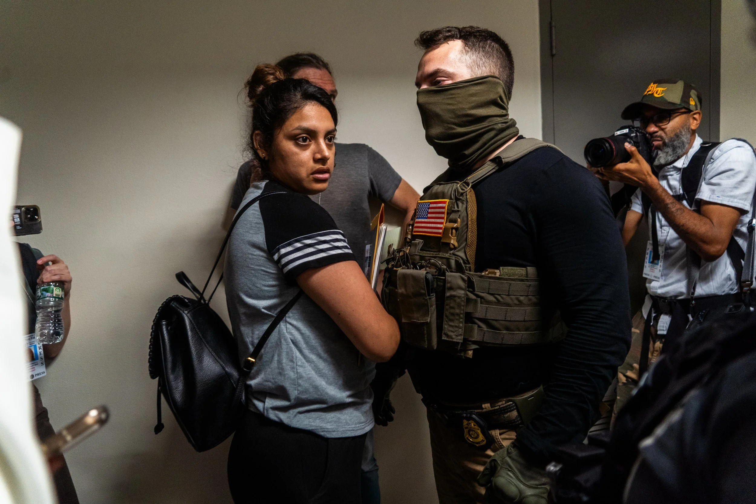 A woman turns to look back, confused and concerned, as her loved one is taken by ICE. He doesn’t speak English. She tries to follow, hoping to translate — but federal agents block her path. Her face holds the weight of helplessness.
