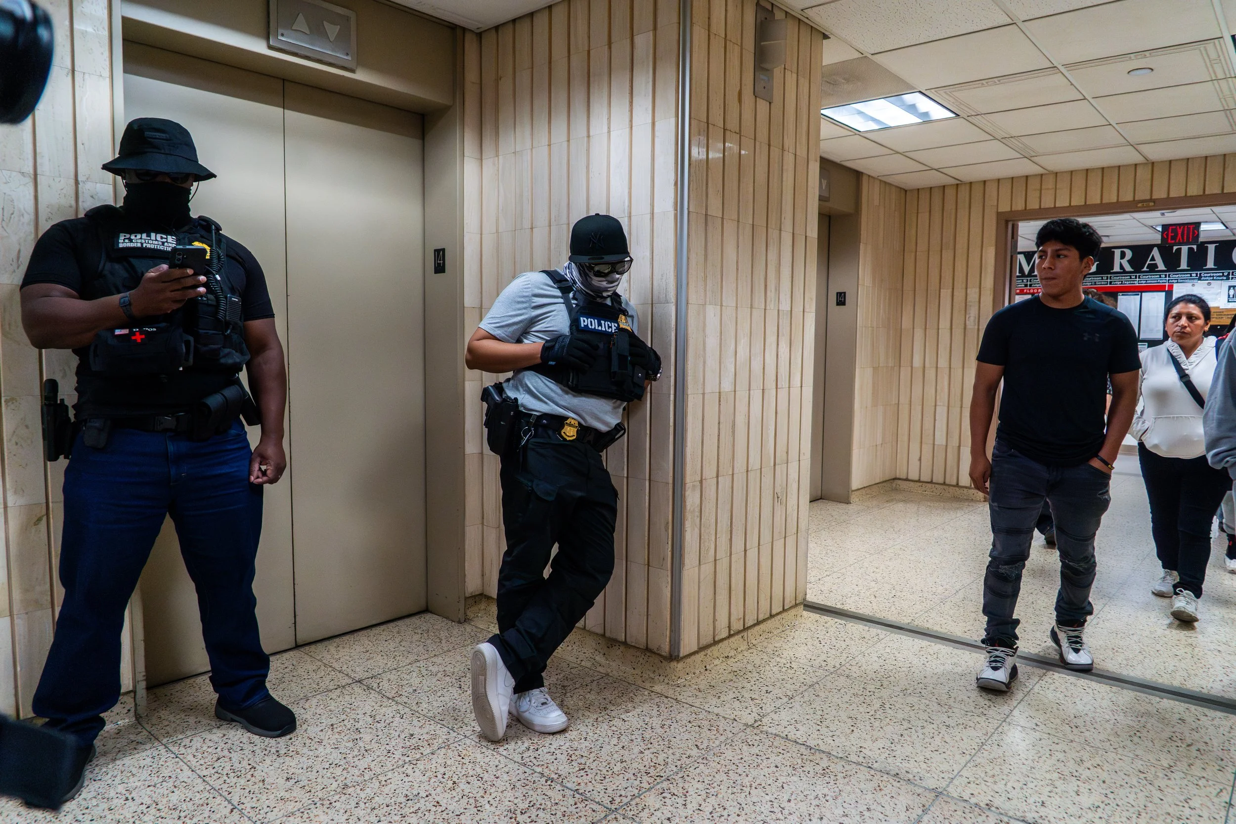 After their hearings, people walk tentatively past ICE agents posted outside the immigration courtroom. One agent leans asleep against the wall.