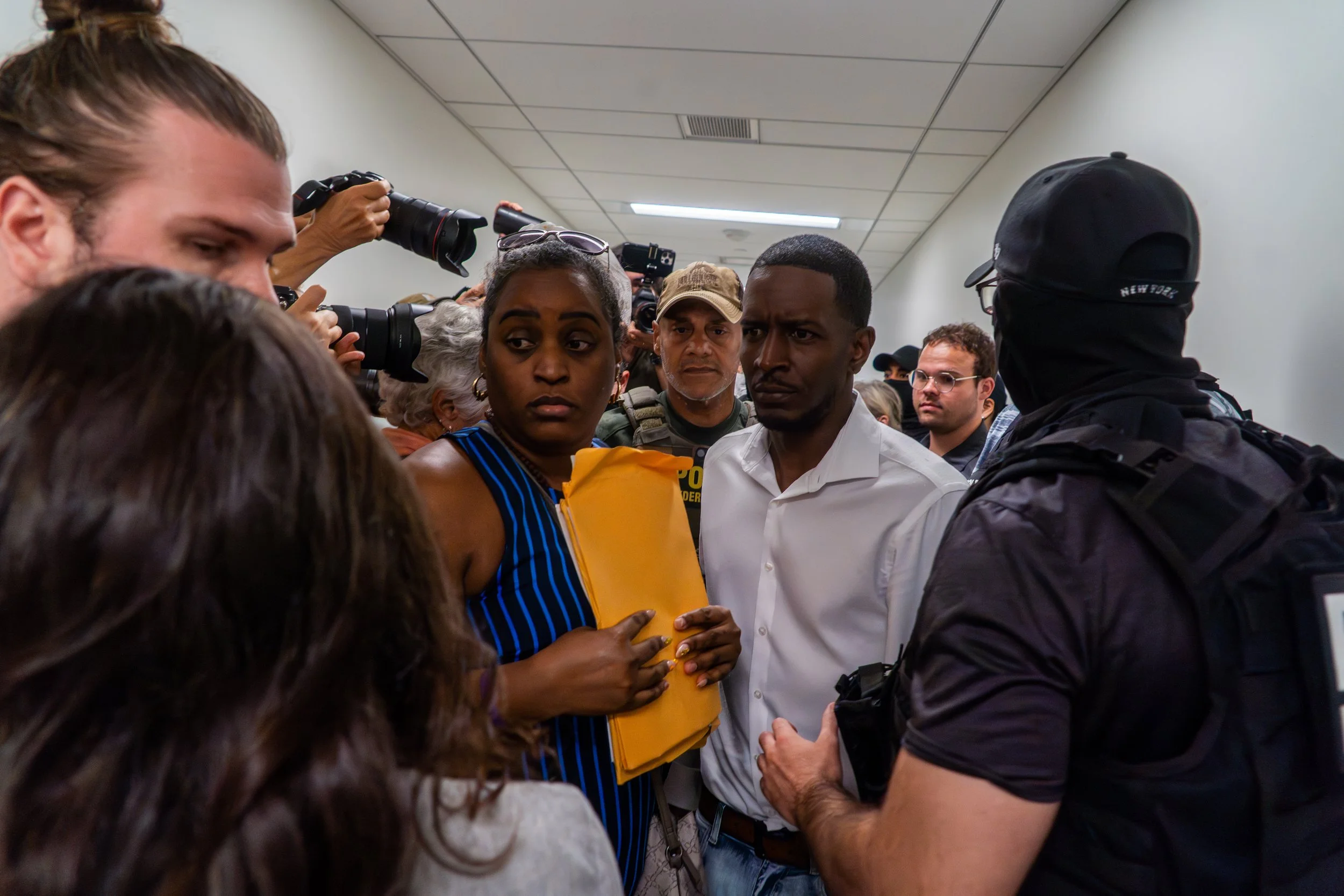 A man is detained in the middle of a crowded hallway. The tension in the room shifts as ICE agents close in — onlookers stop, watching, frozen.