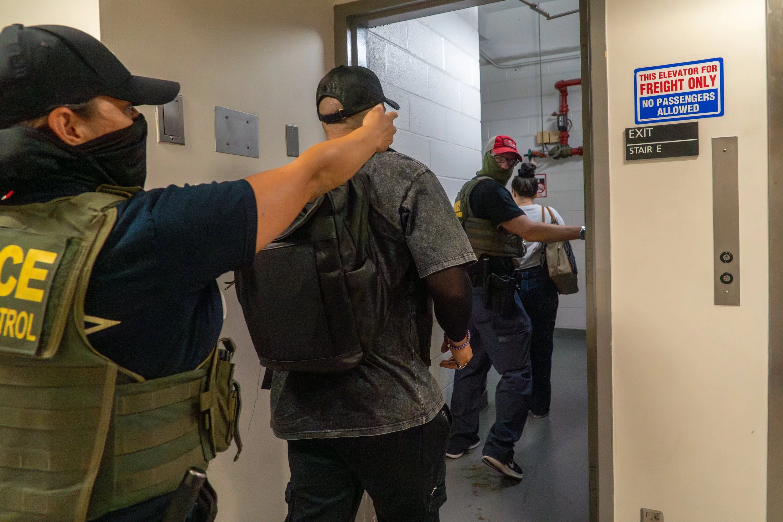 Three ICE agents lead a young girl toward the stairwell.