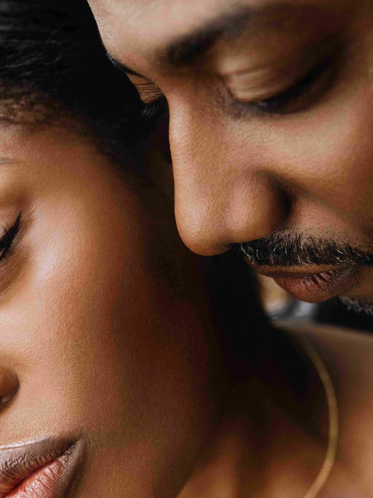 Close-up photo of a man and woman with their foreheads touching and eyes closed, showing intimacy.
