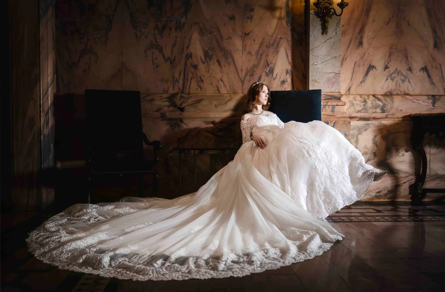 A woman in a wedding dress sitting on a bench in an elegant room with marble walls.