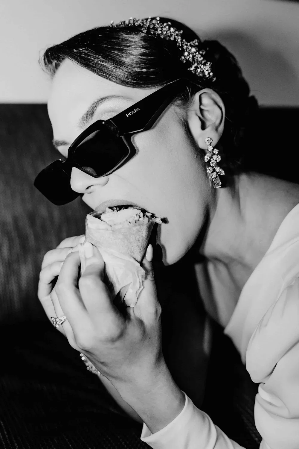 A woman wearing large sunglasses and earrings is eating a slice of pizza.