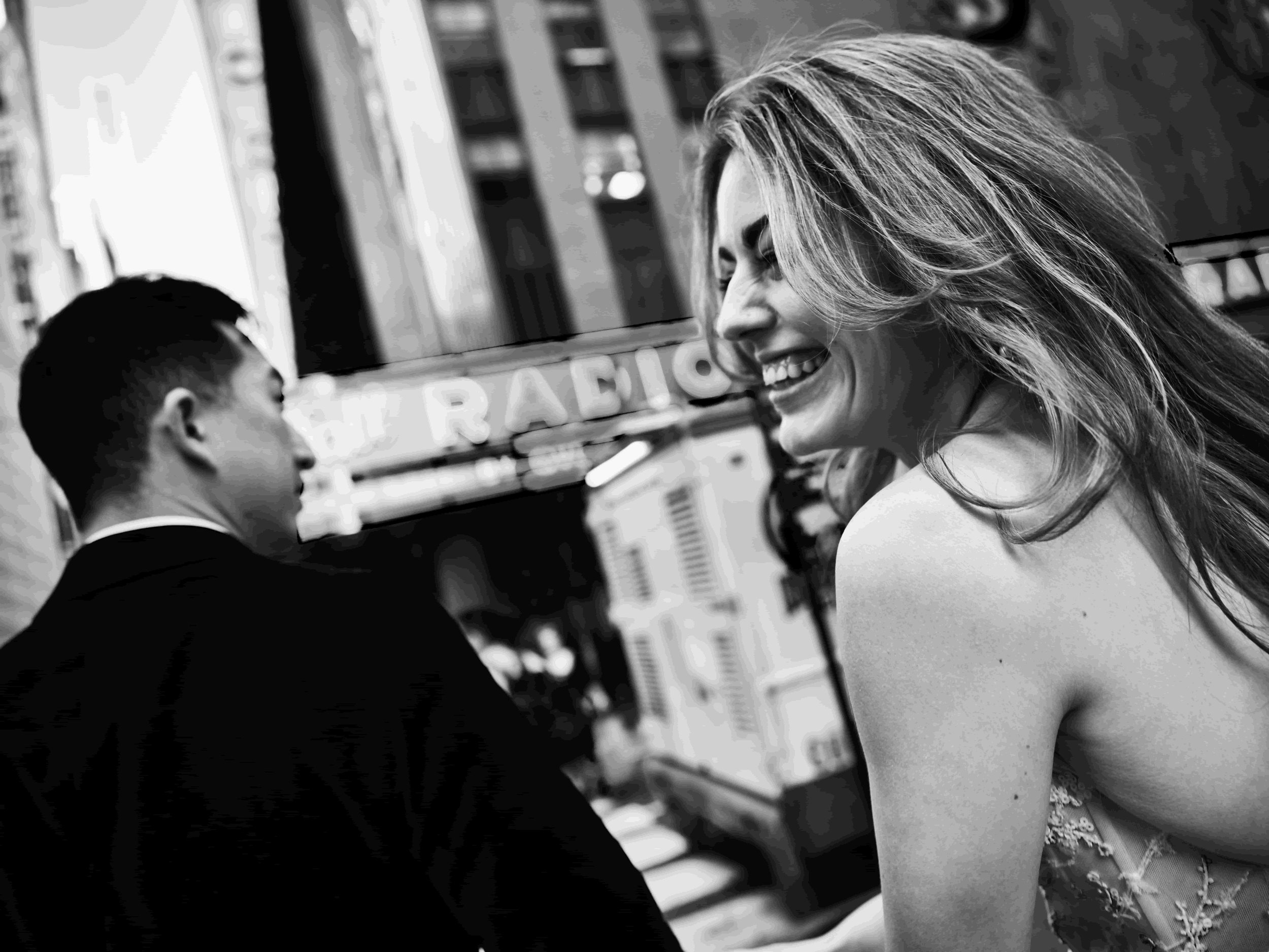 A black-and-white photo of a woman smiling and looking to the side, with a man in the background.