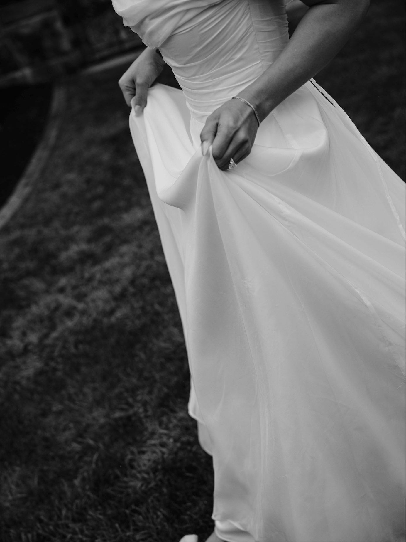 A bride in a wedding dress adjusting her gown outdoors.