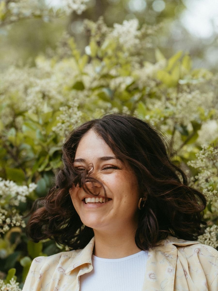 Young woman smiling and twirling in front of a hedge