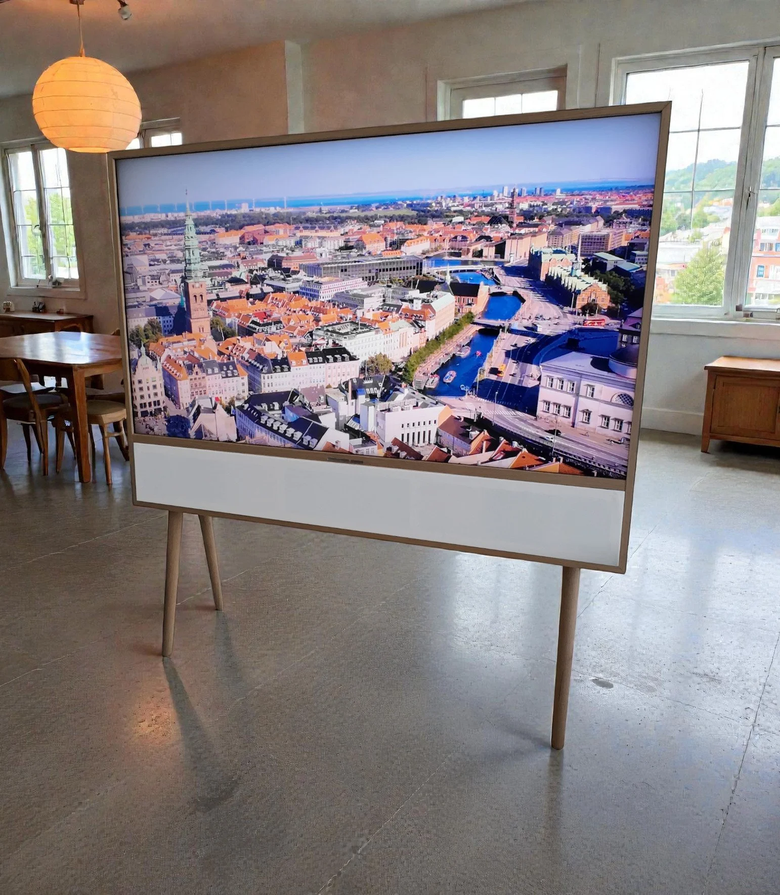 Large digital display screen showing an aerial view of a cityscape with historic buildings, waterways, and modern infrastructure inside a room with wooden furniture, windows, and a paper lantern.