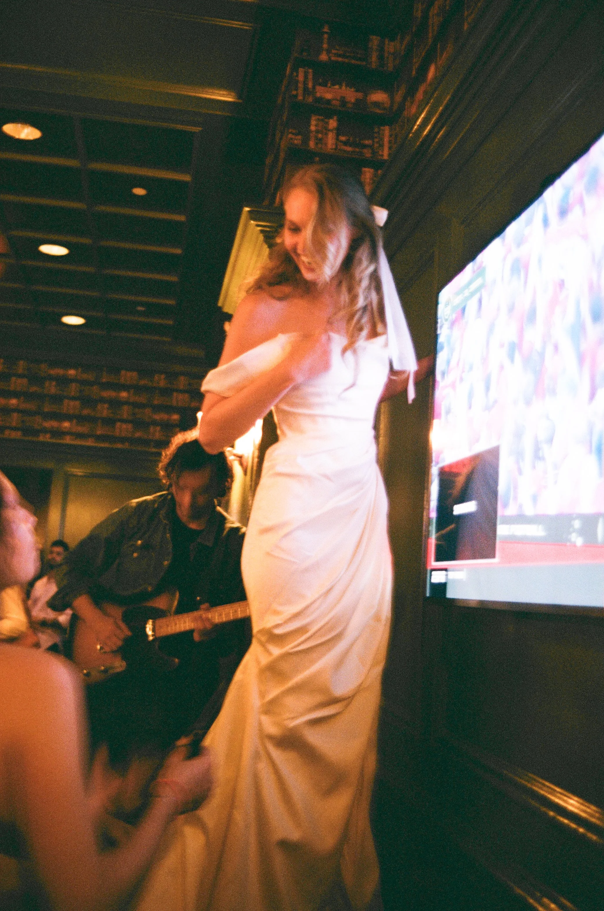Woman in a white gown dancing at an indoor event with a man playing guitar beside her.
