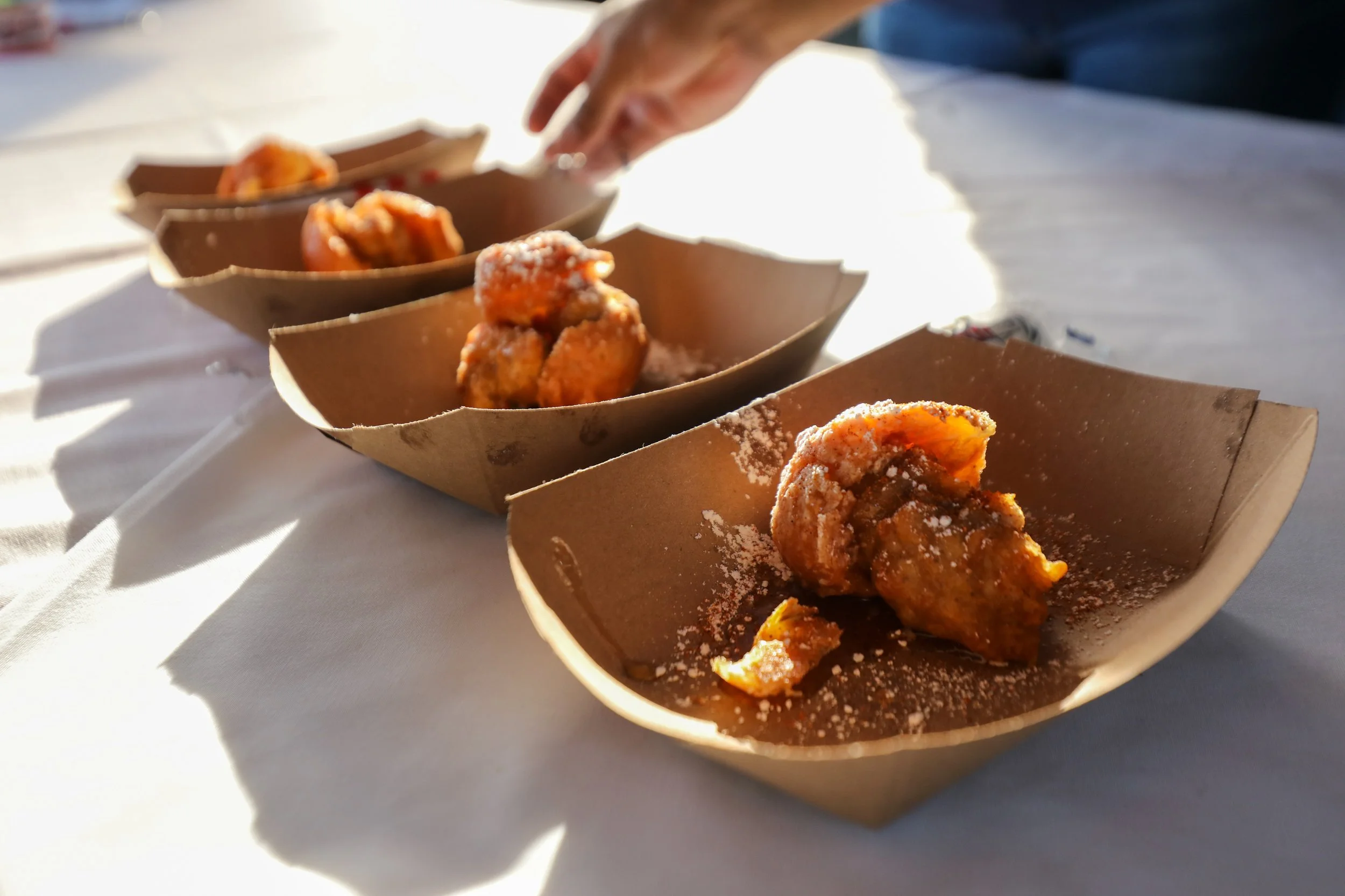 Three people standing behind a table with Little Caesars branding, displaying baked goods, hats, and promotional materials at an event.
