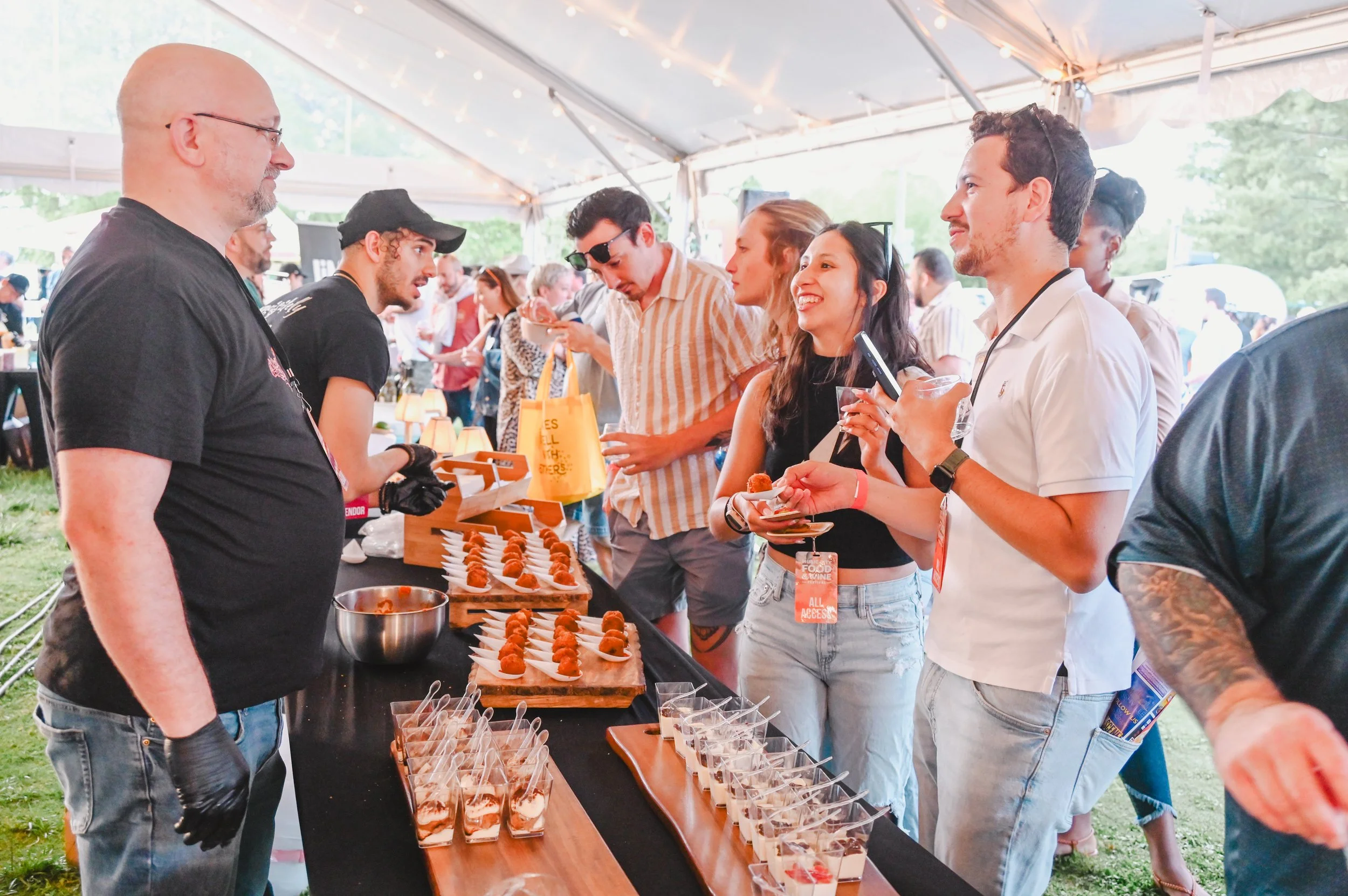 Three people standing behind a table with Little Caesars branding, displaying baked goods, hats, and promotional materials at an event.