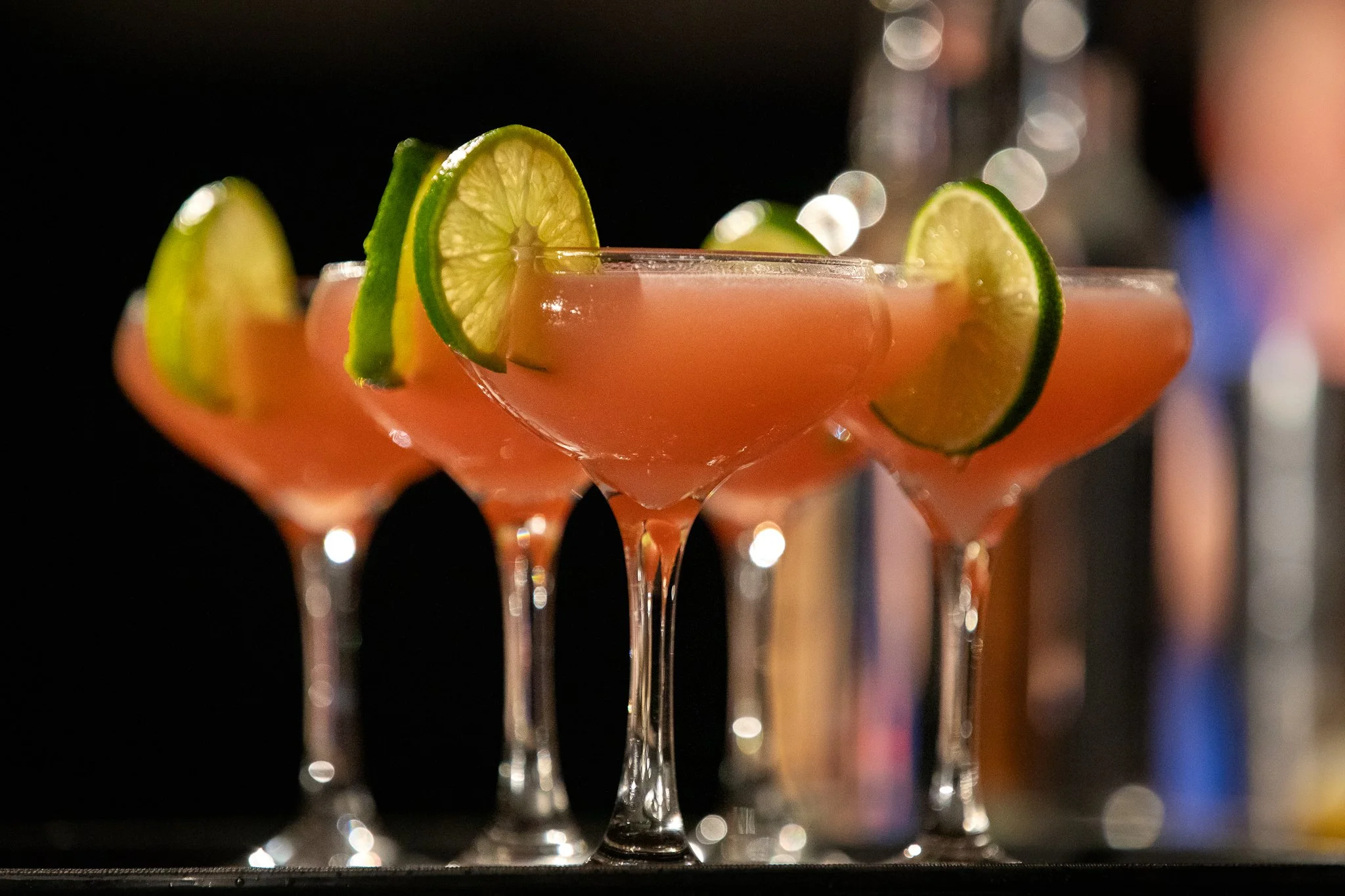 Clear plastic cups filled with pink-colored vodka drinks on a black tray with orange accents, branded with 'Tito's Handmade Vodka' and 'Austin Texas'.