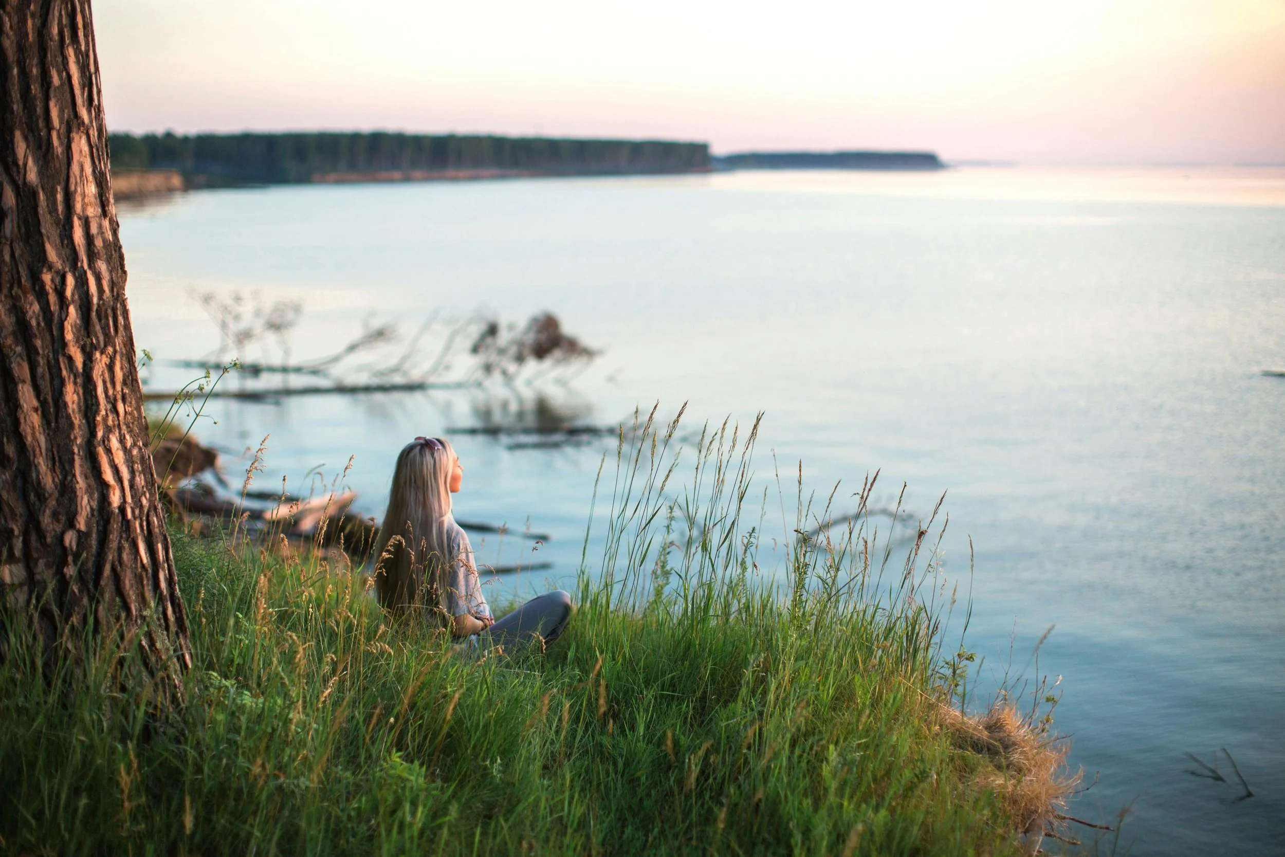woman sitting peacefully by a lake at sunset