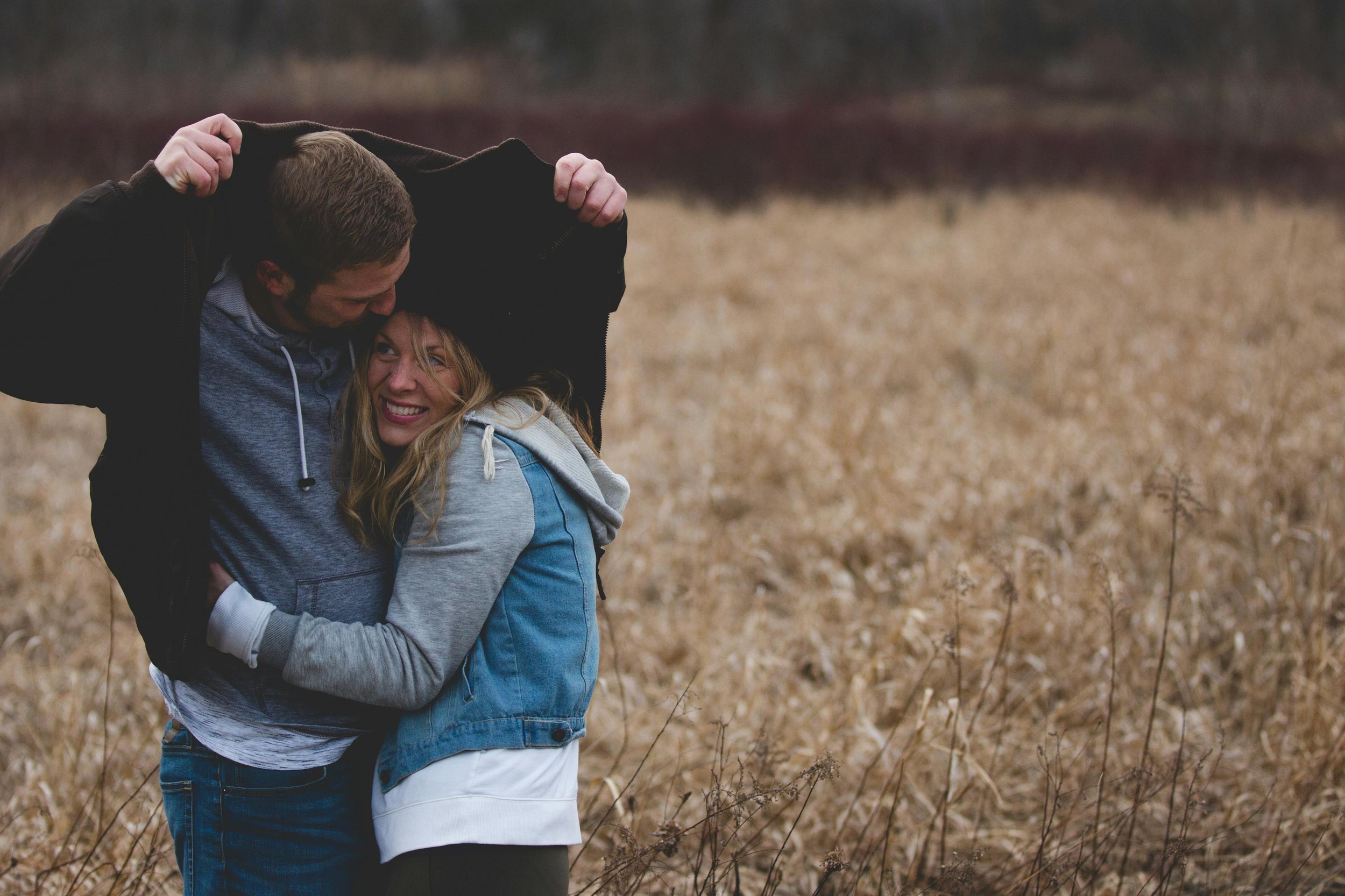 man protecting woman with his jacket in a field