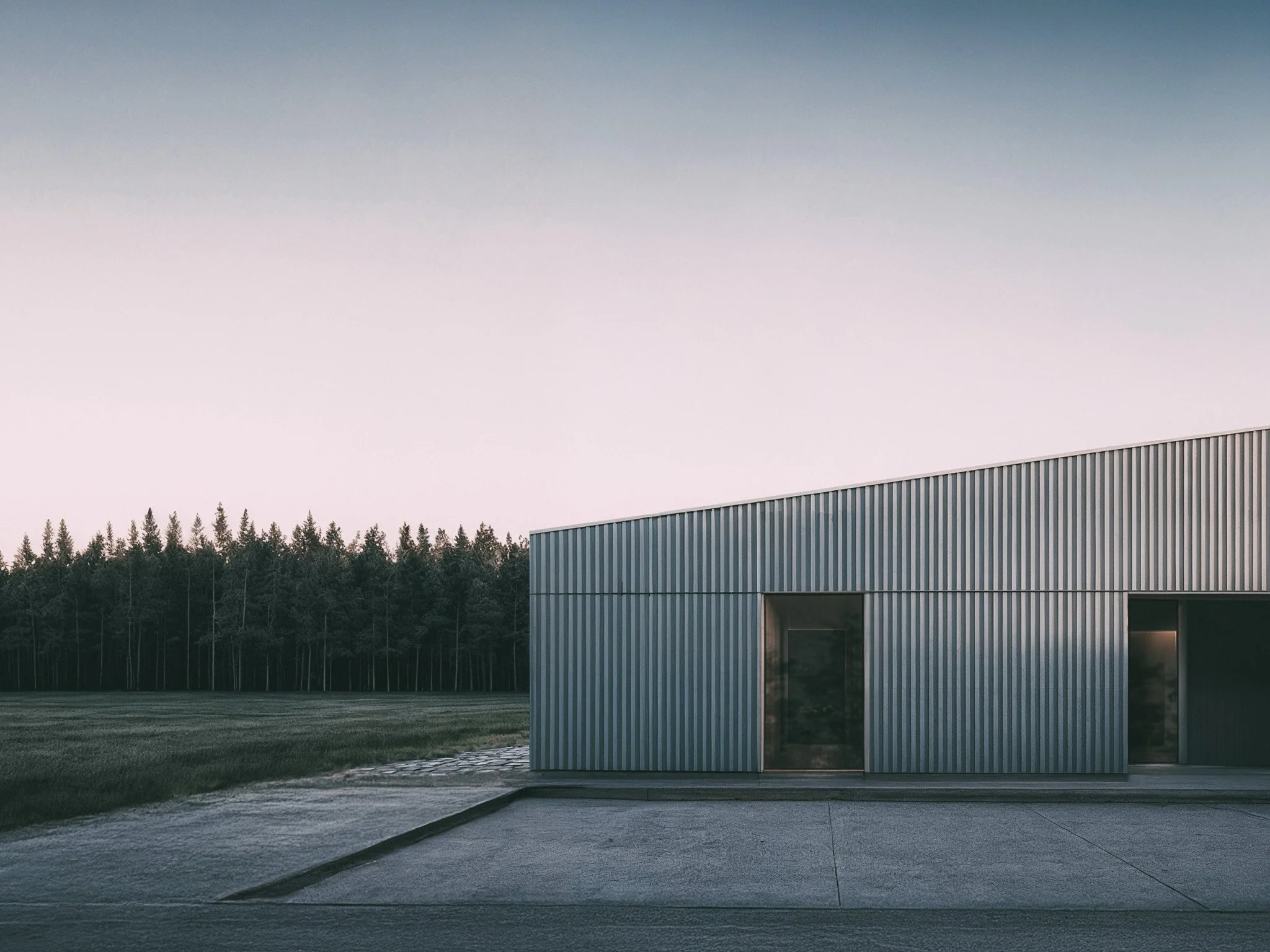 Bâtiment moderne en métal avec deux portes, situé dans un paysage avec des arbres en arrière-plan, sous un ciel clair.