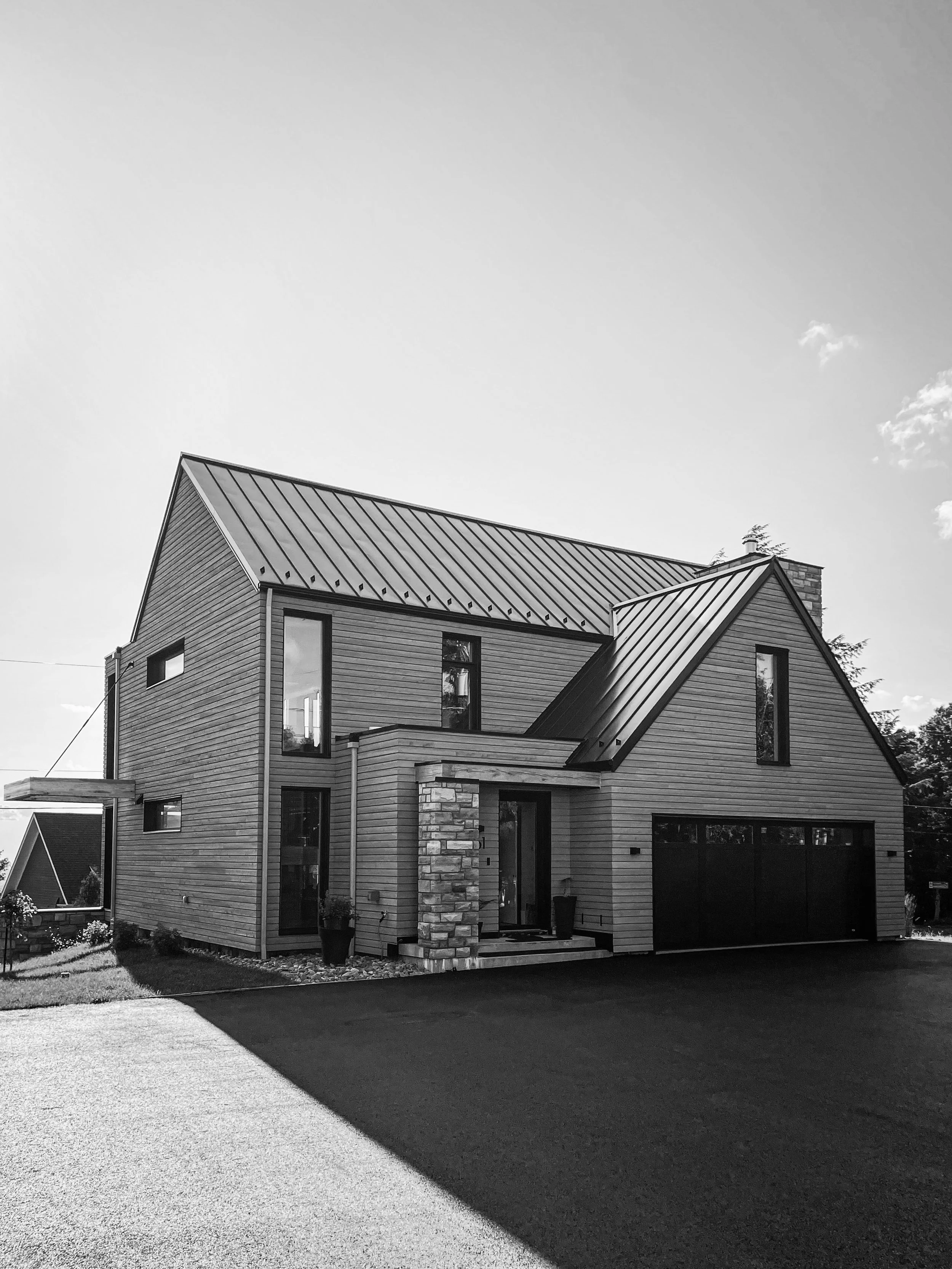 Maison moderne en bois avec un toit en métal, deux étages, et un grand garage, vue monochrome.