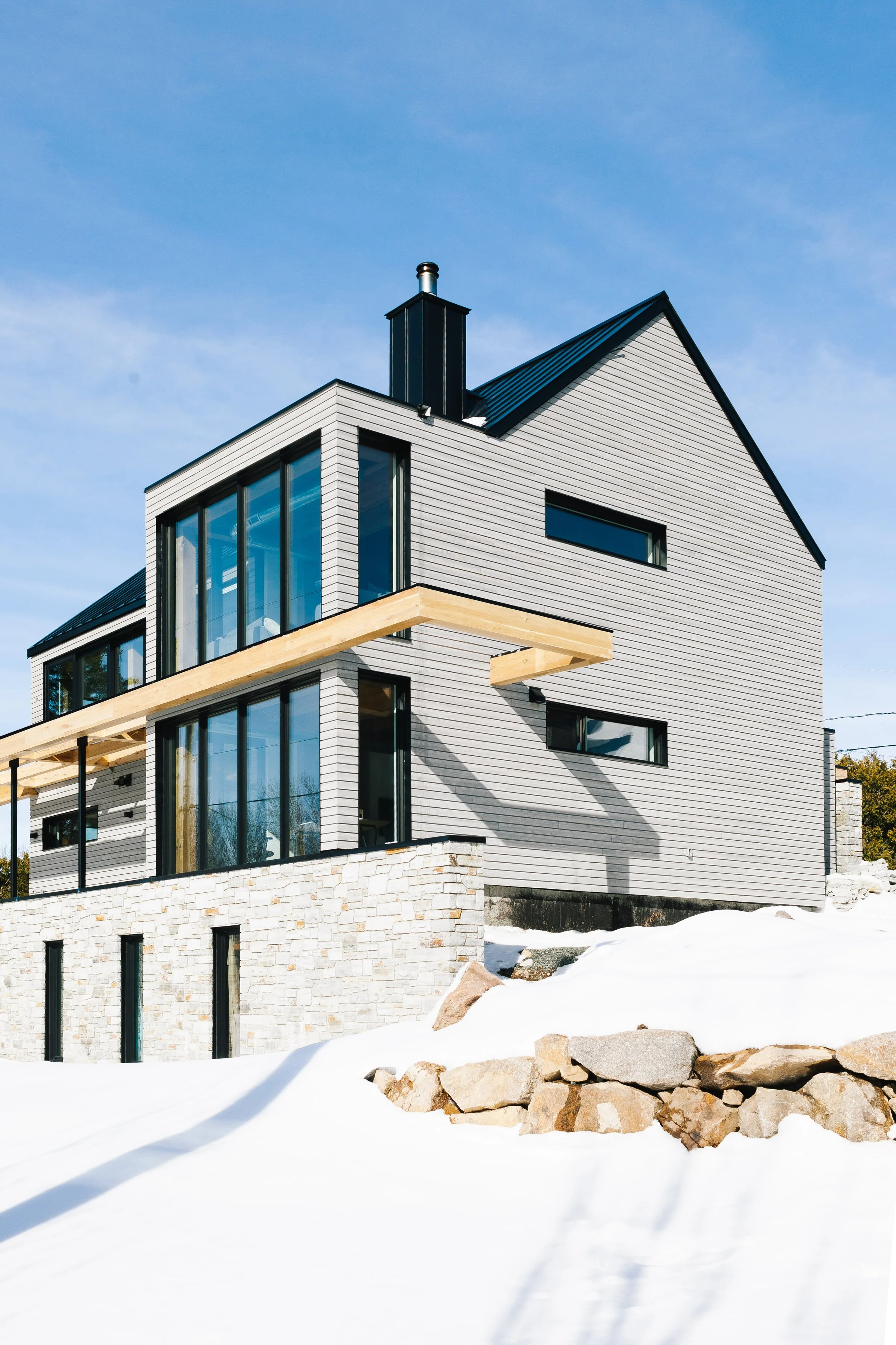 Maison moderne en bois et pierre construite sur un terrain enneigé avec un ciel bleu clair