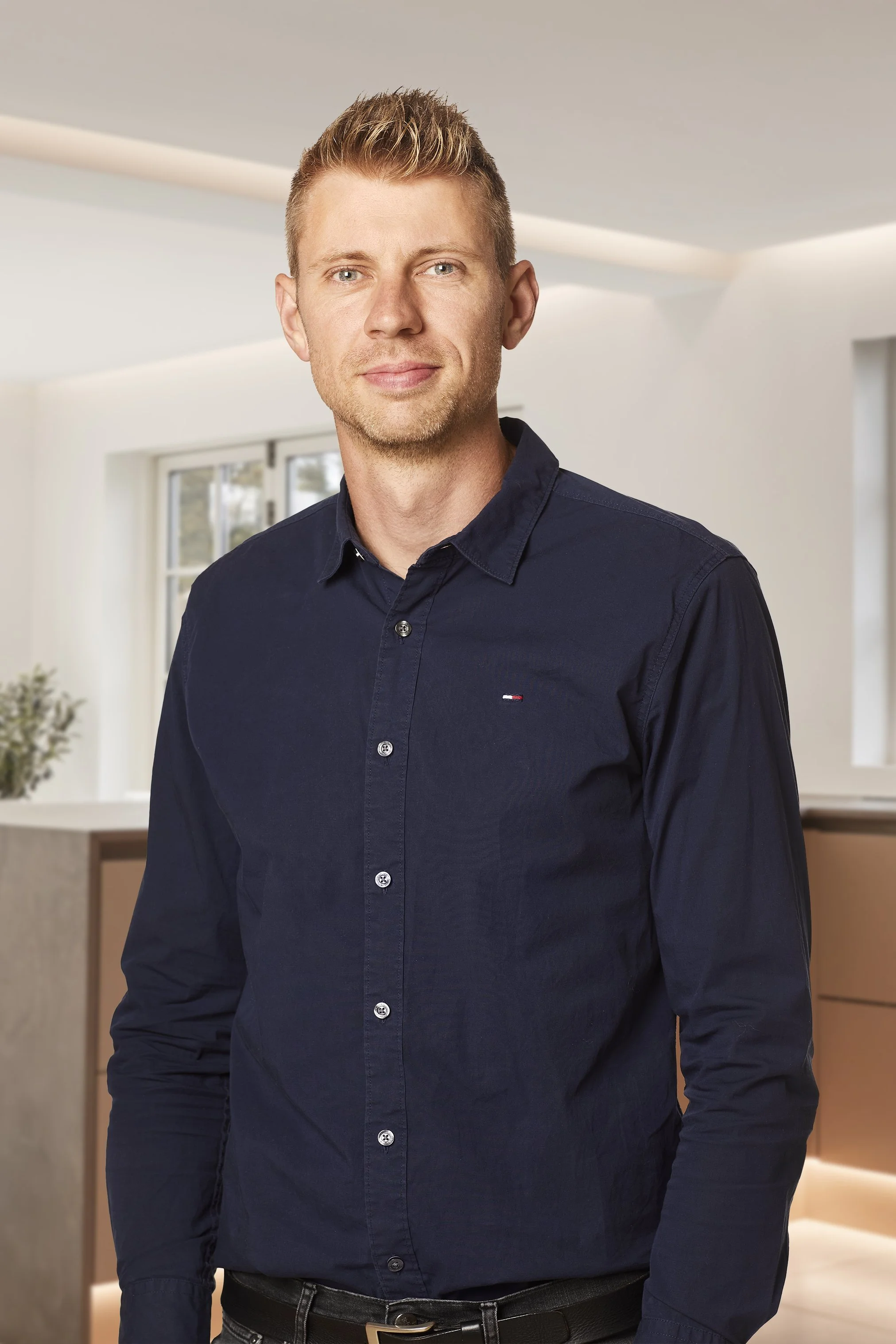 En ung mand i jakkesæt smilende indendørs.