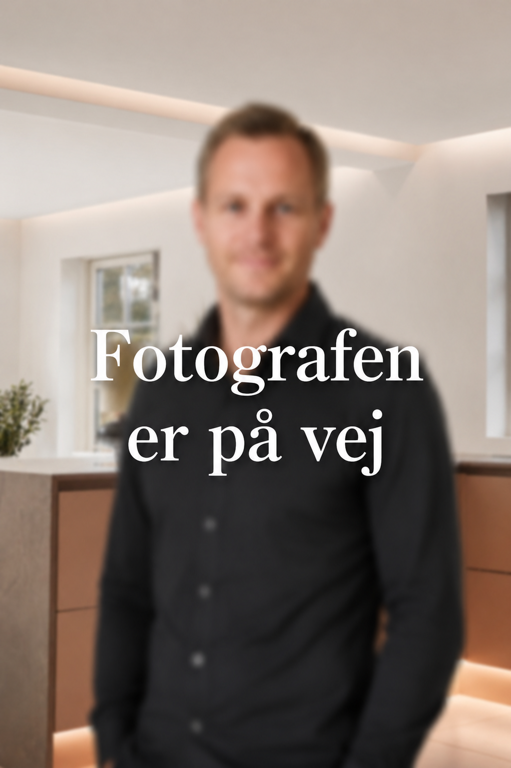 En ung mand i jakkesæt smilende indendørs.