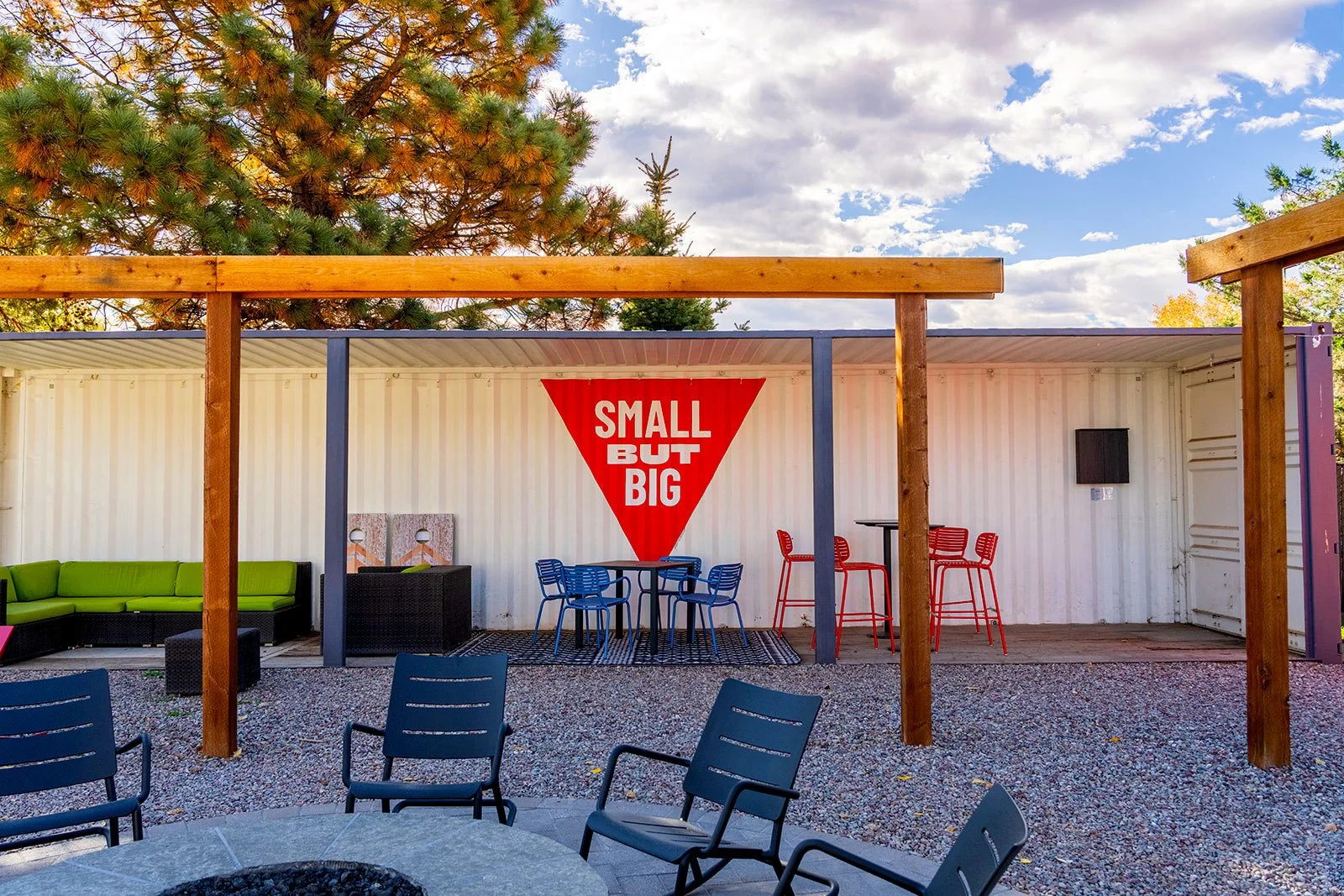Shipping container common area with "Small But Big" graphic, lounge seating, and cornhole at Tiny Town

A shared outdoor lounge built into a repurposed shipping container gives Tiny Town residents a covered gathering space, complete with the "Small B