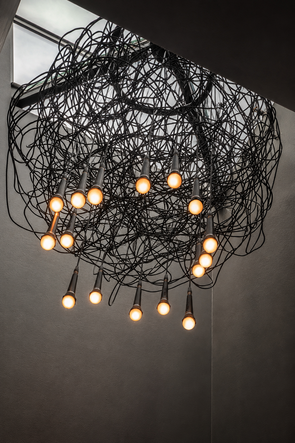 Sculptural wire pendant chandelier hanging beneath a skylight at the Paul JAS Center Caption: Custom sculptural lighting installation at the Paul JAS Center, a tangled wire-and-bulb chandelier suspended beneath a rooftop skylight, part of Monoco's br