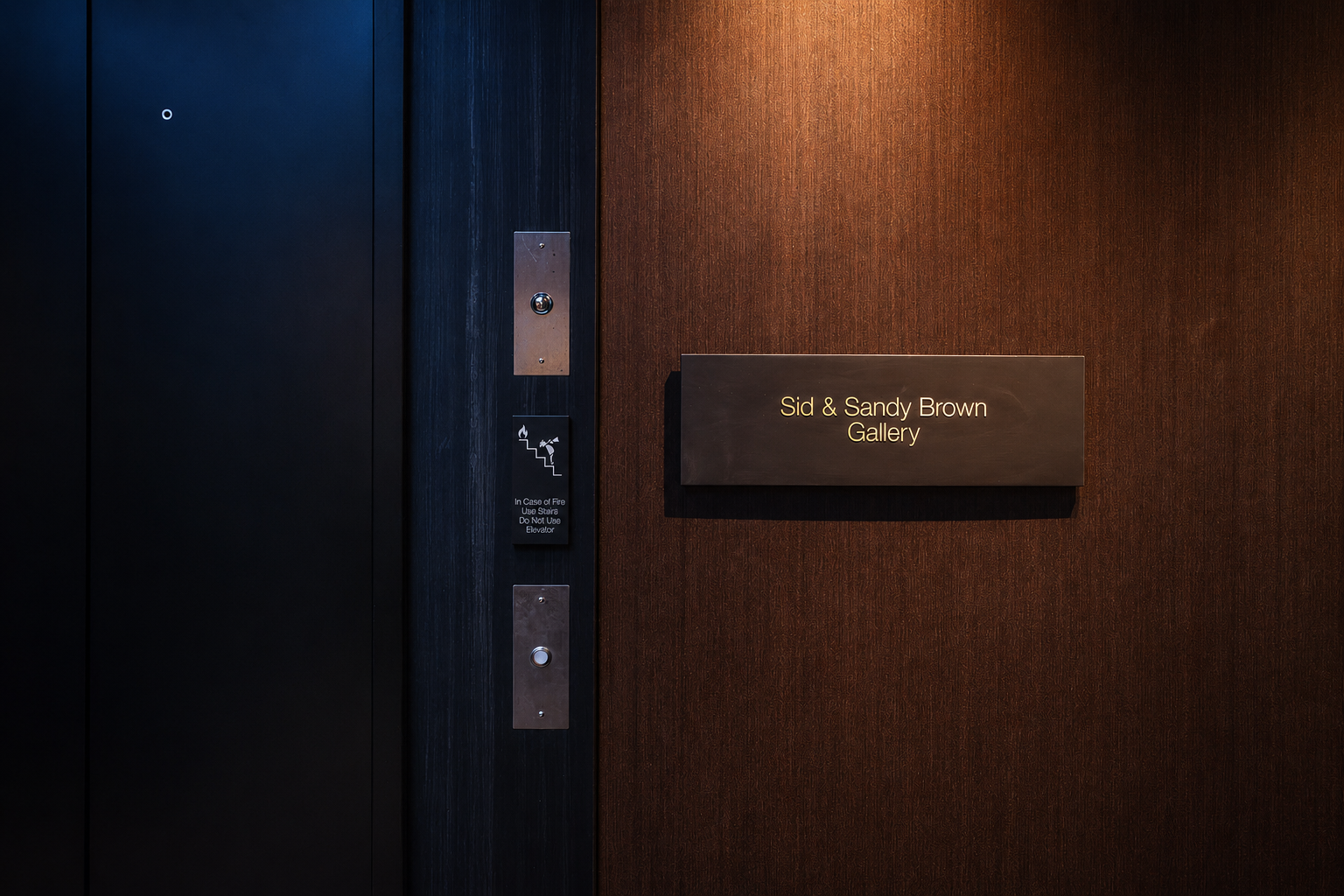 Sid & Sandy Brown Gallery donor plaque beside elevator at the Paul JAS Center Caption: Named donor room plaque for the Sid & Sandy Brown Gallery at the Paul JAS Center, mounted on wood paneling adjacent to the venue's elevator and stair signage.