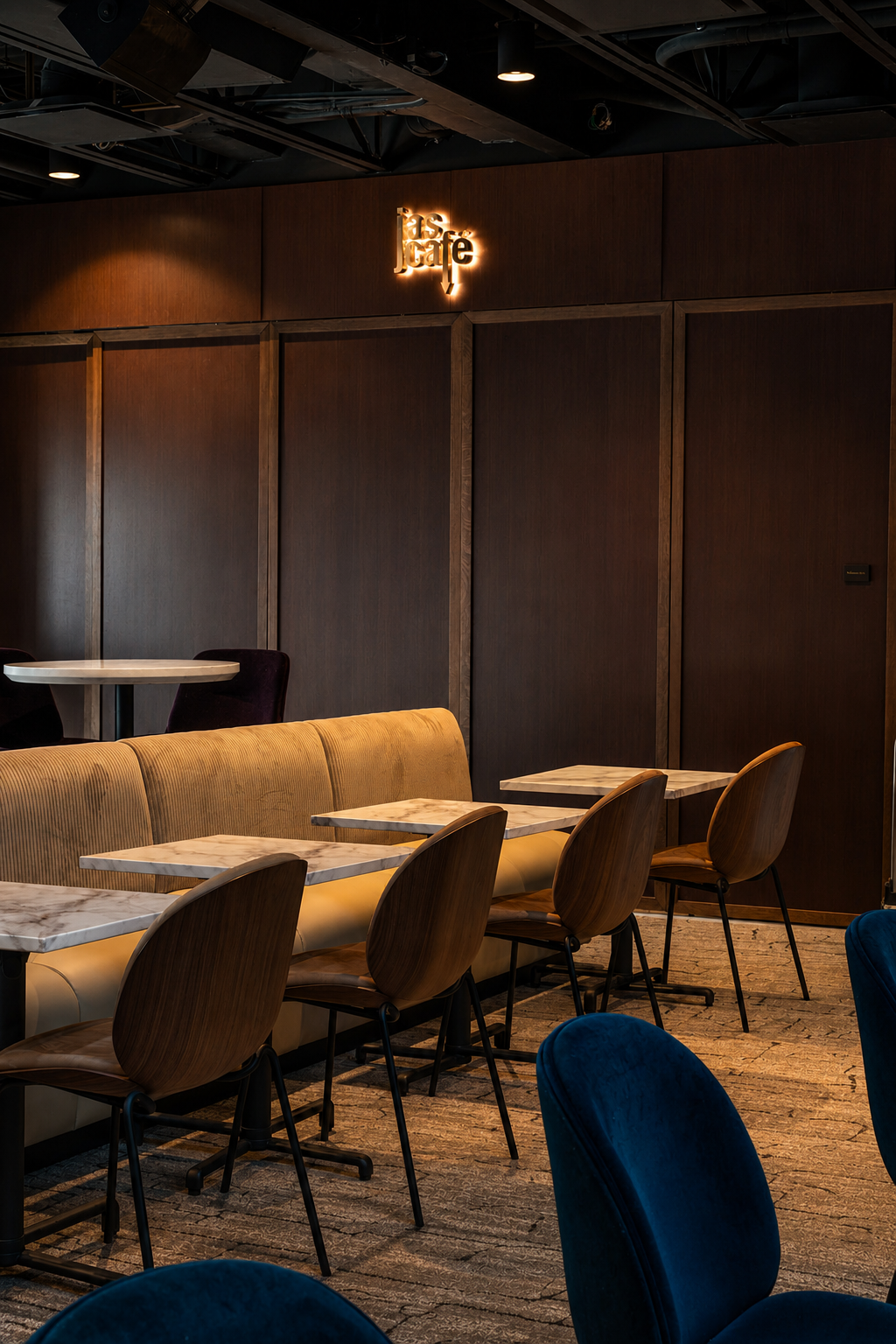 Backlit "JAS Café" logo sign above wood-paneled booth seating at the Paul JAS Center Caption: Custom backlit logo signage for the JAS Café inside the Paul JAS Center, integrated into dark wood paneling above velvet booth seating and marble café table