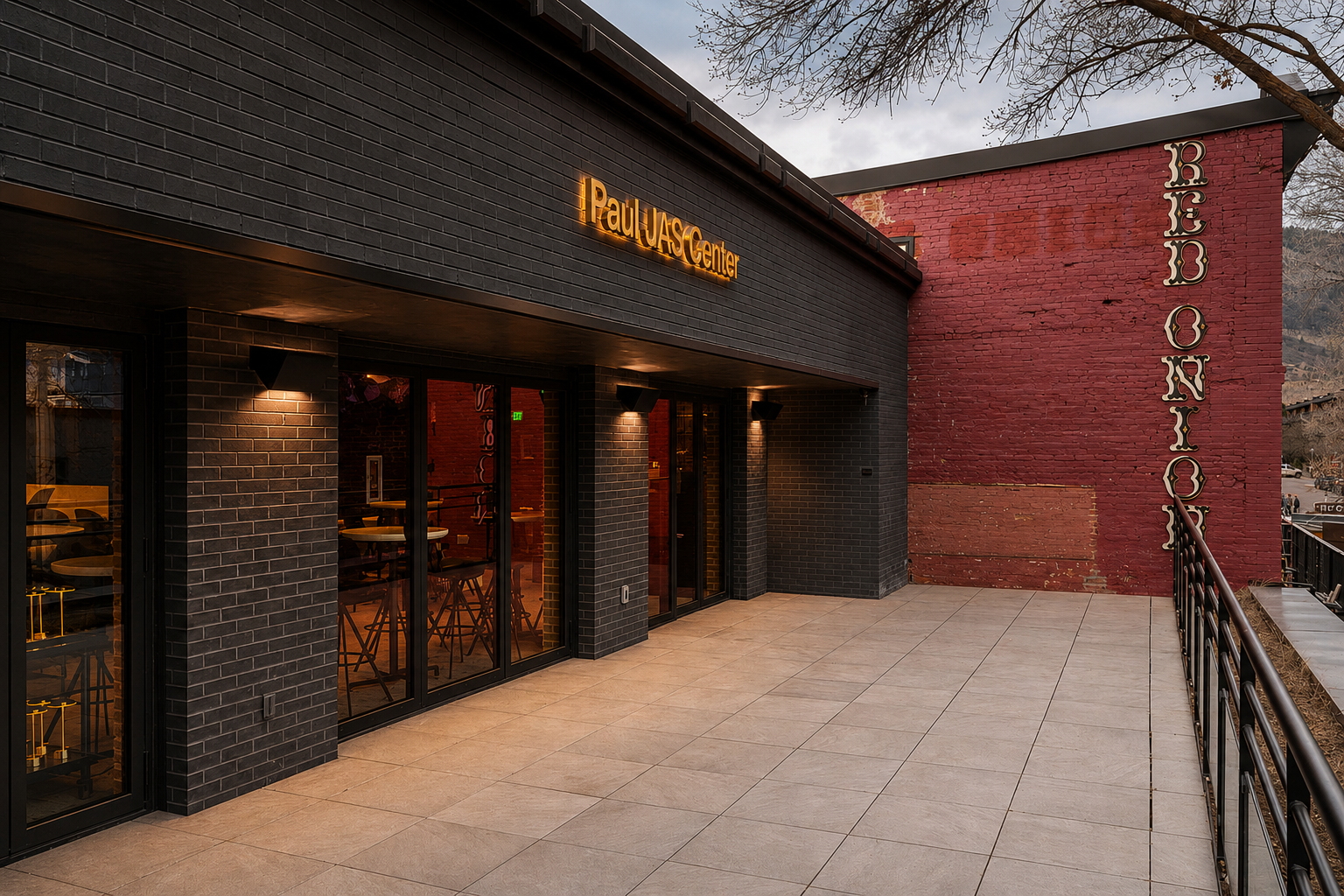 Paul JAS Center exterior sign on black brick facade beside the historic Red Onion building in Aspen, Colorado Caption: Illuminated exterior building-identification signage for the Paul JAS Center, mounted on dark brick above the venue's glass entry d
