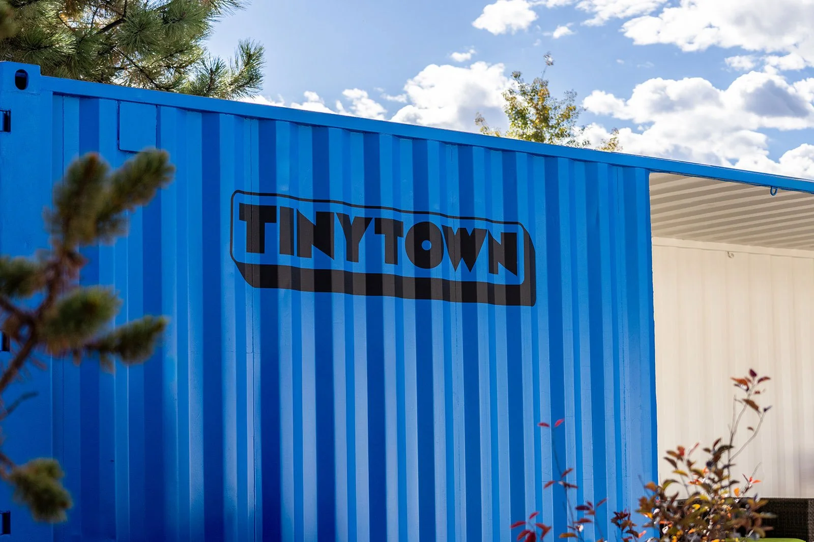 Blue shipping container with black "Tinytown" wordmark signage

A blue shipping container at Tiny Town displays the community's bold outlined wordmark, one of several branded containers repurposed for storage and amenity space.