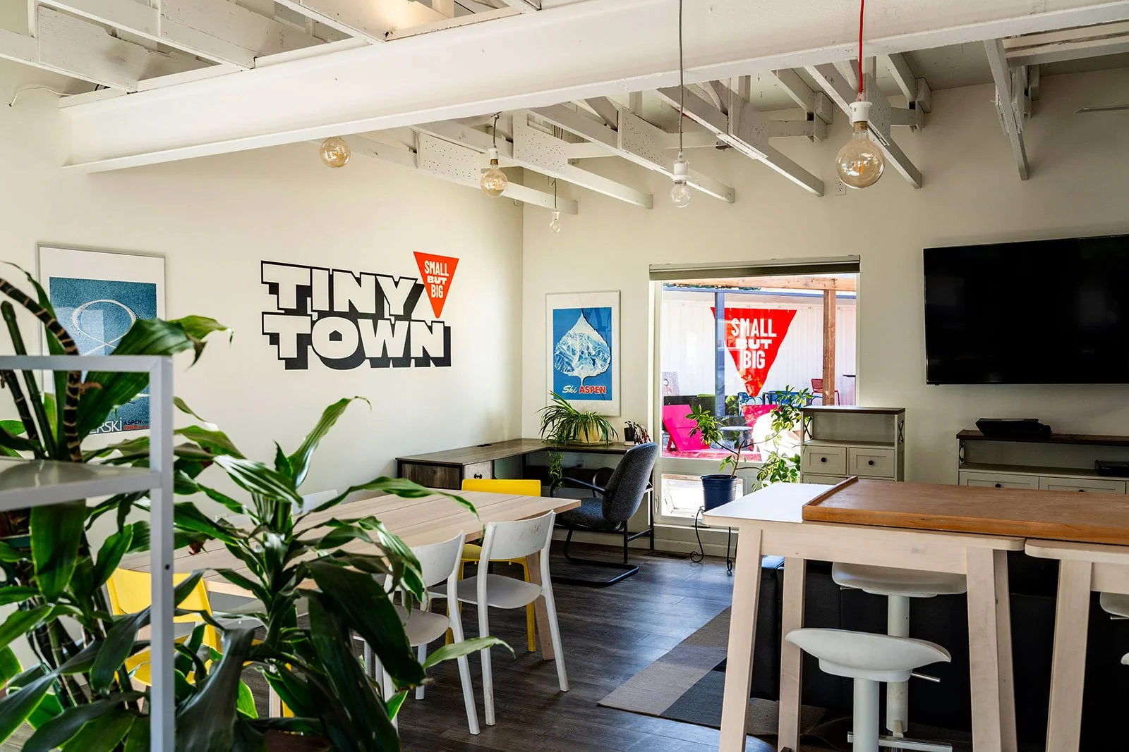Tiny Town clubhouse interior with wordmark wall graphic, lounge seating, and kitchen island

Inside Tiny Town's clubhouse, the "Small But Big" wordmark anchors a light-filled common room with dining tables, a lounge area, and views out to the contain