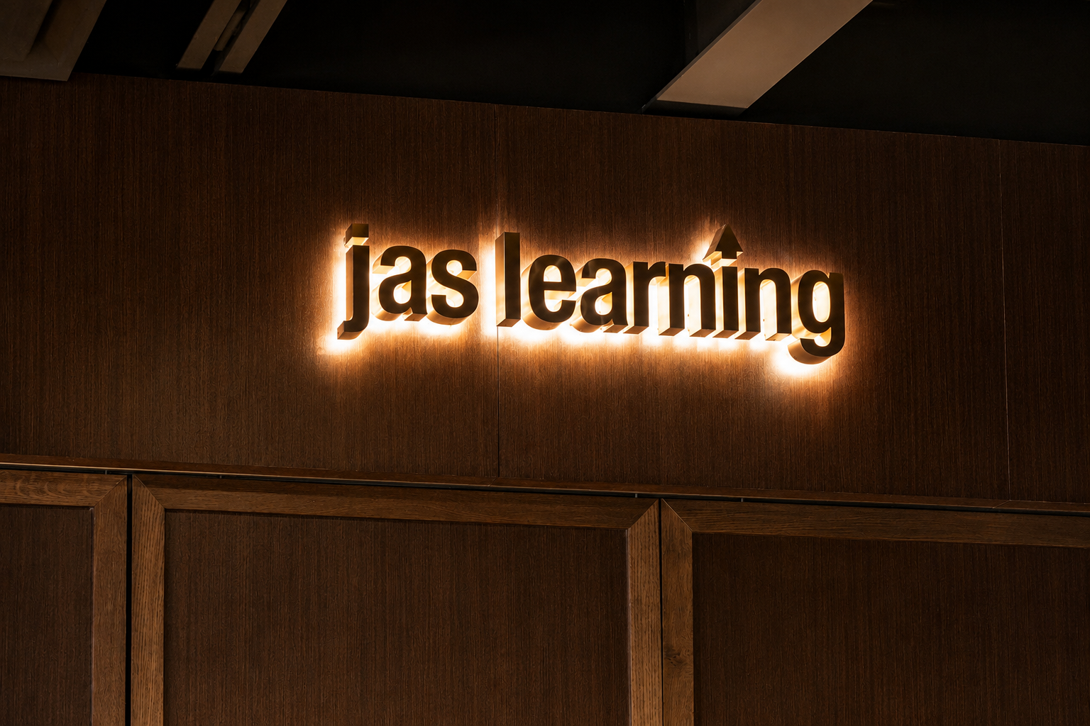Backlit "JAS Learning" sign on wood paneling inside the Paul JAS Center Caption: Custom backlit dimensional signage for JAS Learning, the education program space inside the Paul JAS Center, mounted on dark wood paneling.