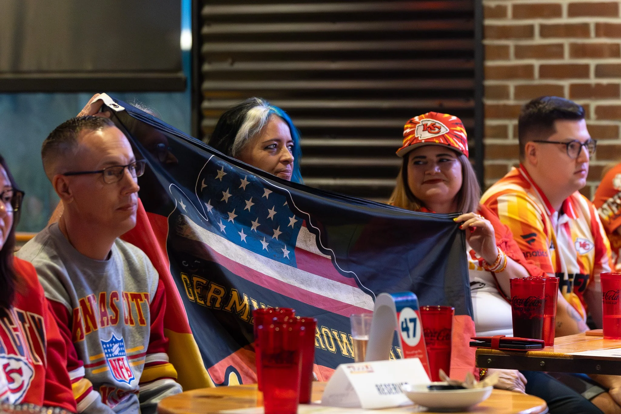 Audience members holding up a flag at the Kansas City Huddle live taping at Chicken N Pickle Overland Park