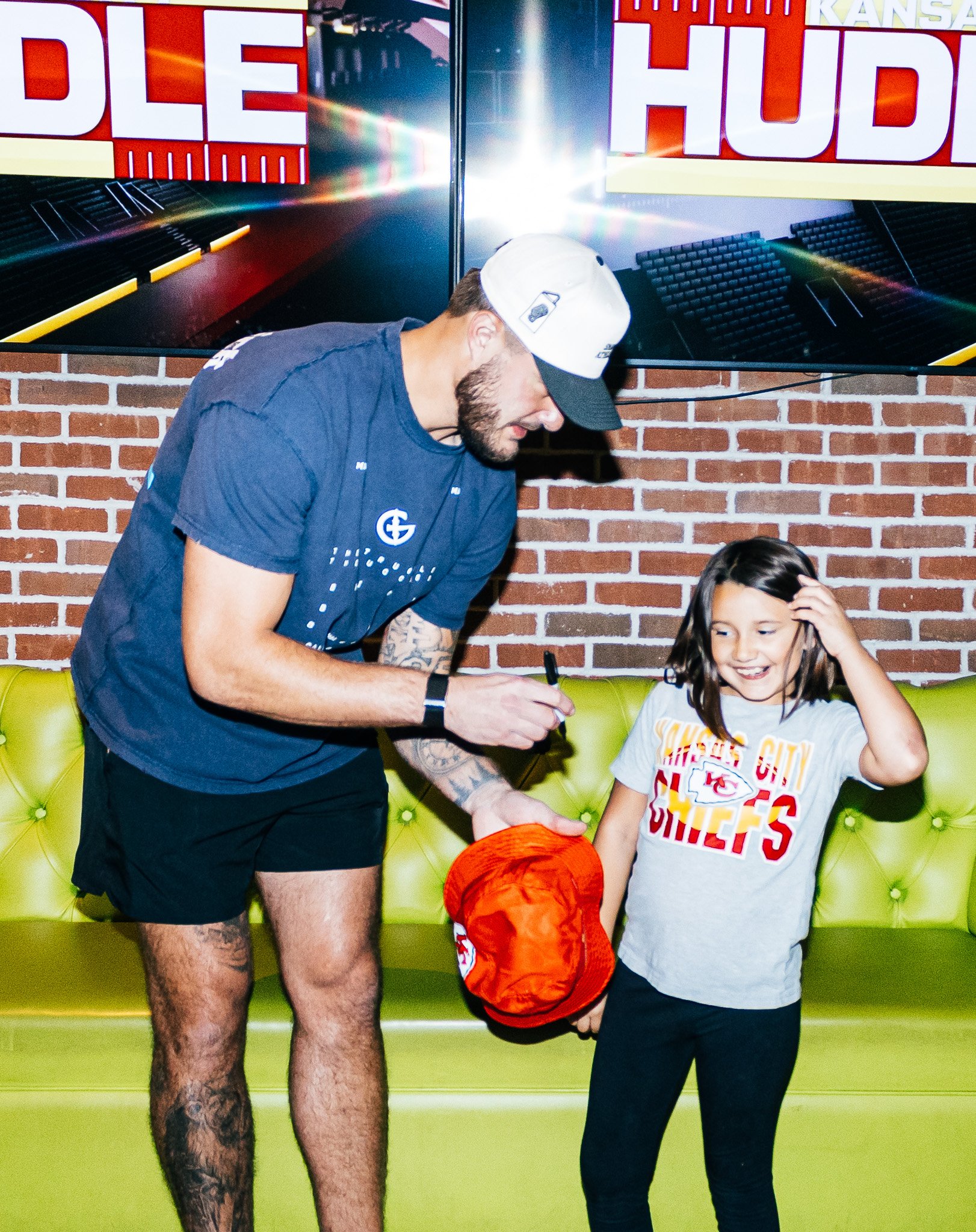 Jared Wiley signs a bucket hat for a young girl at Kansas City Huddle live taping.