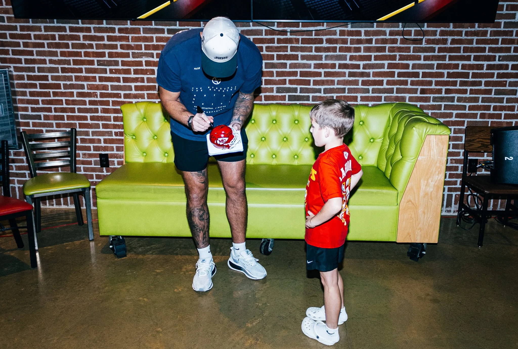 Jared Wiley signs a mini helmet for a young boy at Kansas City Huddle at Chicken N Pickle Overland Park.
