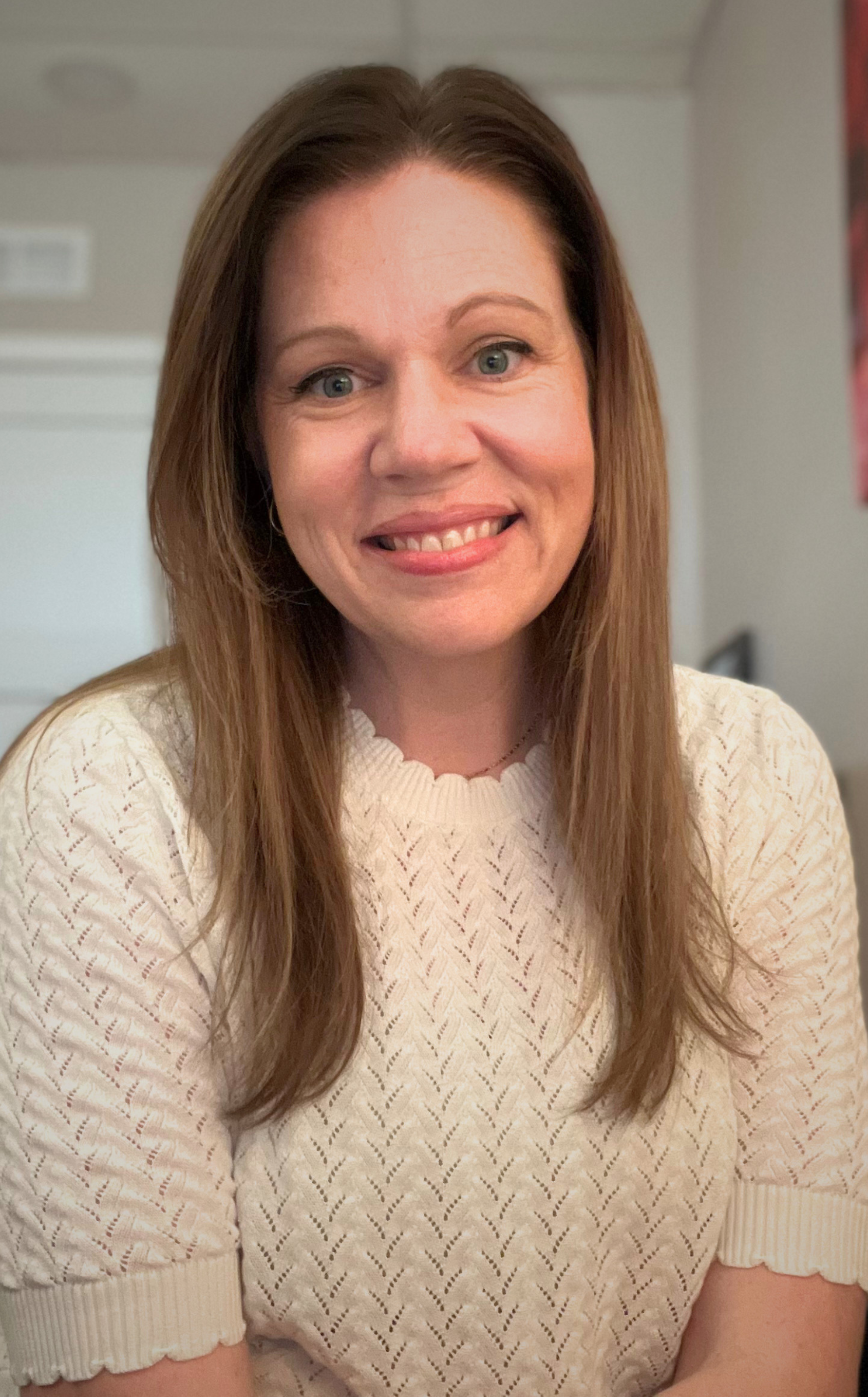 Woman with long hair seated in front of a bookshelf with various books and decor items.