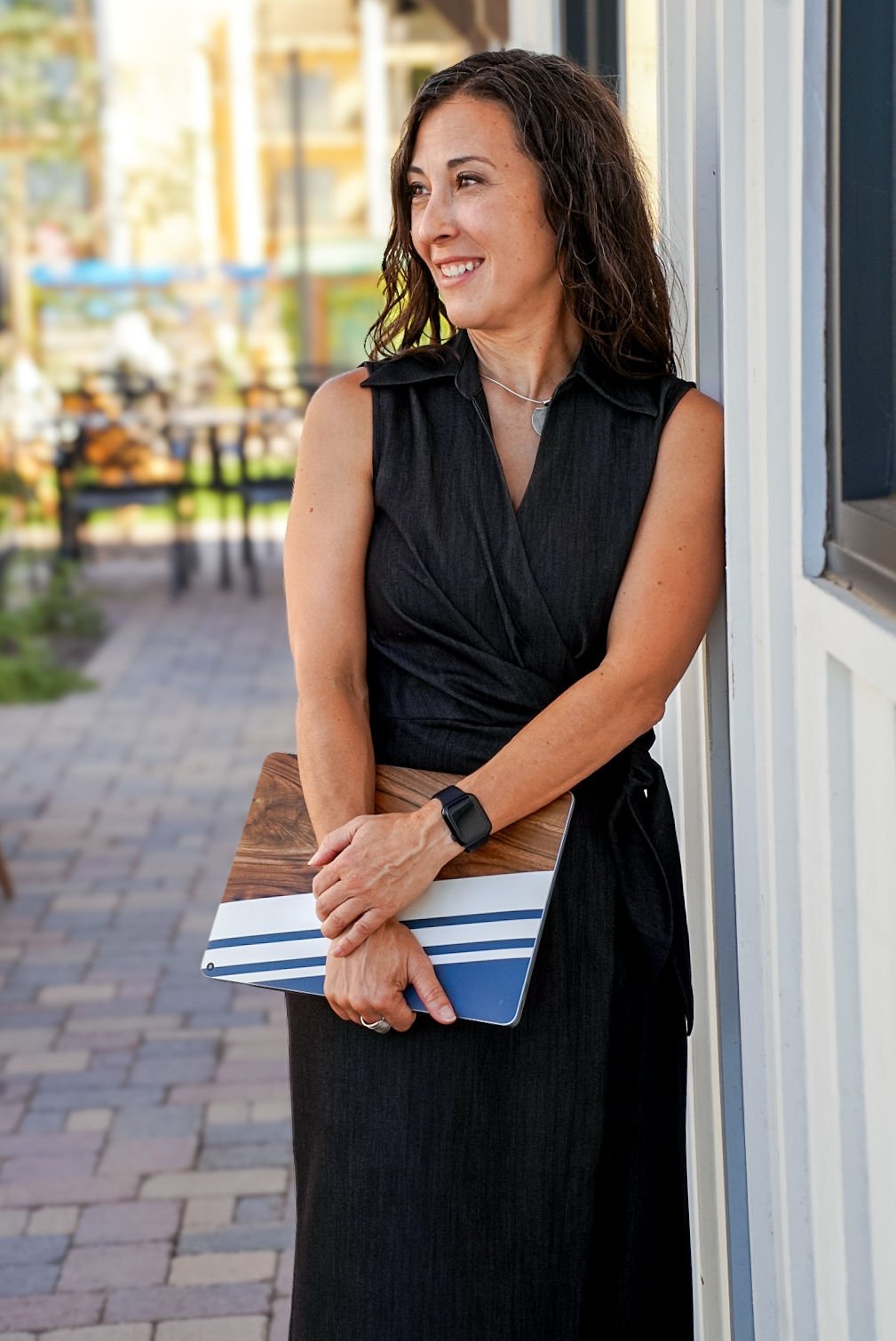 Woman in black dress holding a laptop, standing outdoors against a wall.