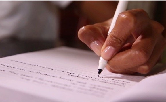 Close-up of a hand holding a white pen and writing on a document on a white paper.