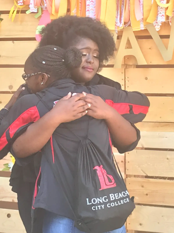 Two people hugging, wearing Long Beach City College attire, with a colorful background.