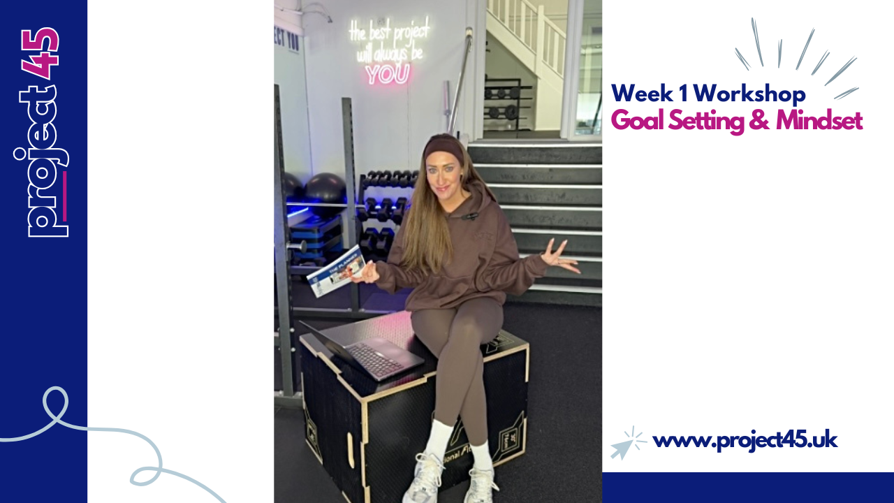 A woman sitting on a black workout box in a gym, holding a phone in one hand and making a peace sign with the other. She wears a brown hoodie, beige leggings, and white athletic shoes. The gym has black exercise balls, weights, and a staircase in the background, with a neon sign that reads 'the best project will always be YOU'. There is text indicating a workshop titled 'Week 1 Workshop Goal Setting & Mindset' with the website www.project45.uk.