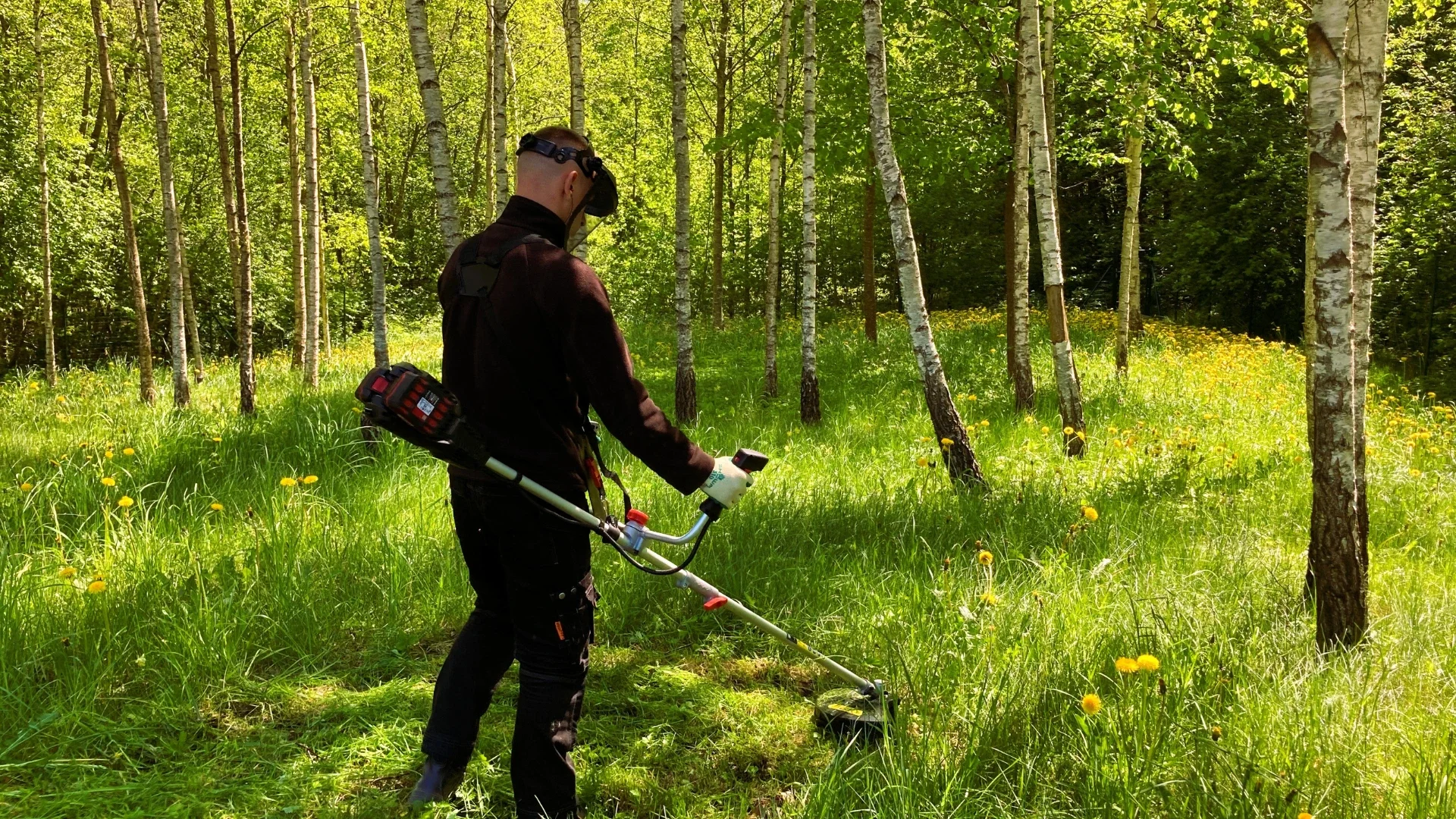Vyrukas pjaunantis aukštą žolę akumuliatoriniu trimeriu.