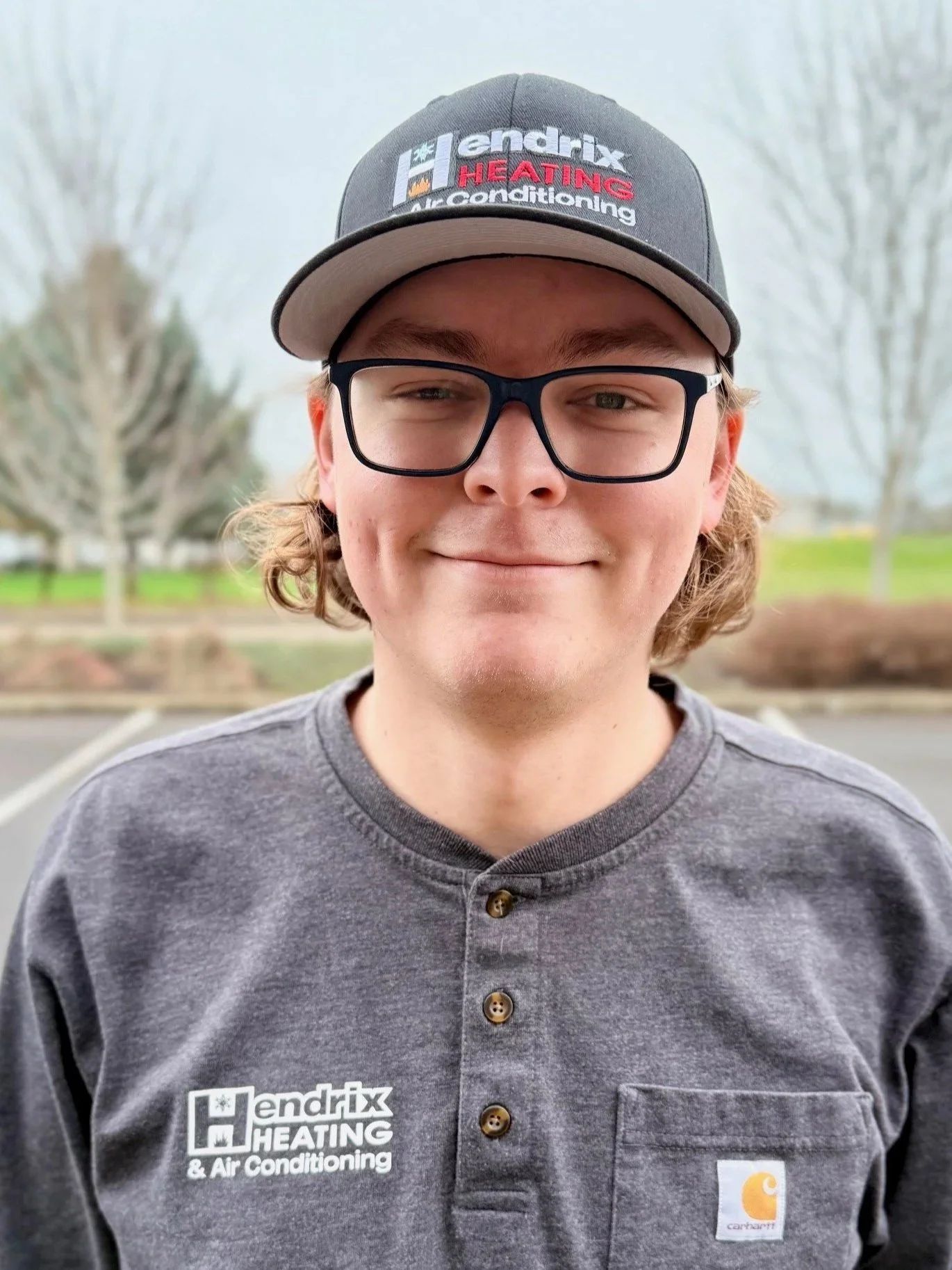 Person wearing glasses and a Hendrix Heating & Air Conditioning shirt and cap, standing outdoors.