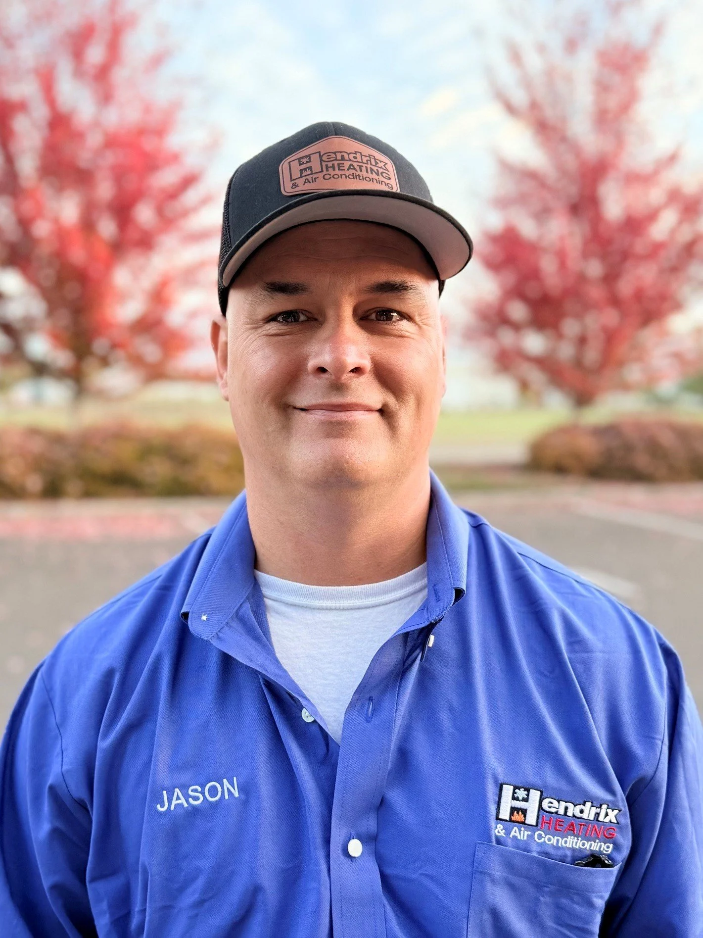 Man in a blue shirt and cap standing outdoors with trees and blurred background.