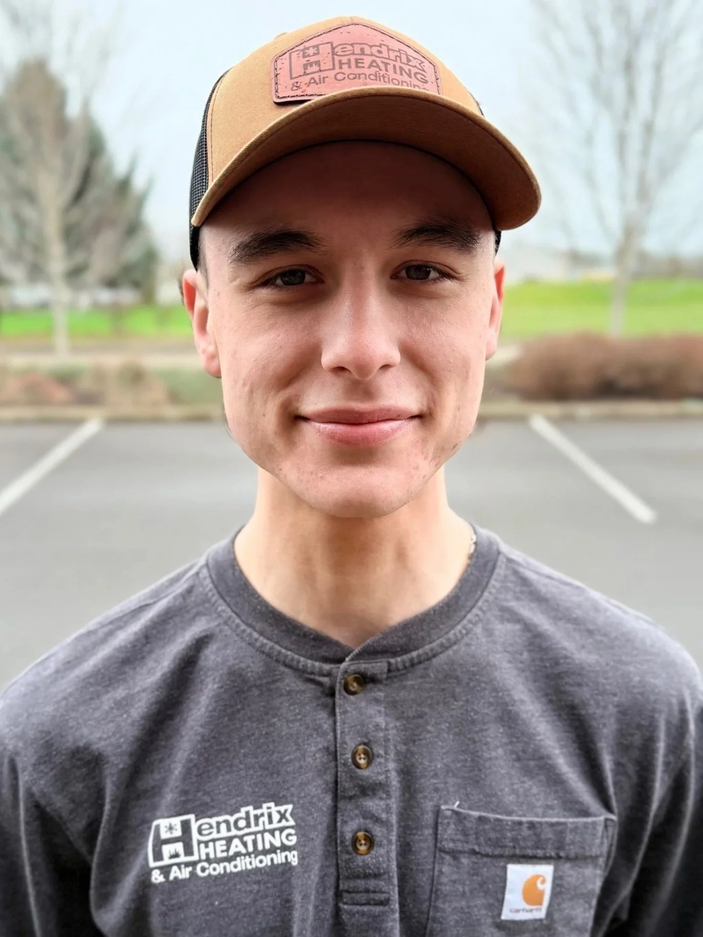 Person wearing a black hoodie with "Hendrix Heating Est. 1952" logo standing outdoors with autumn trees in the background.