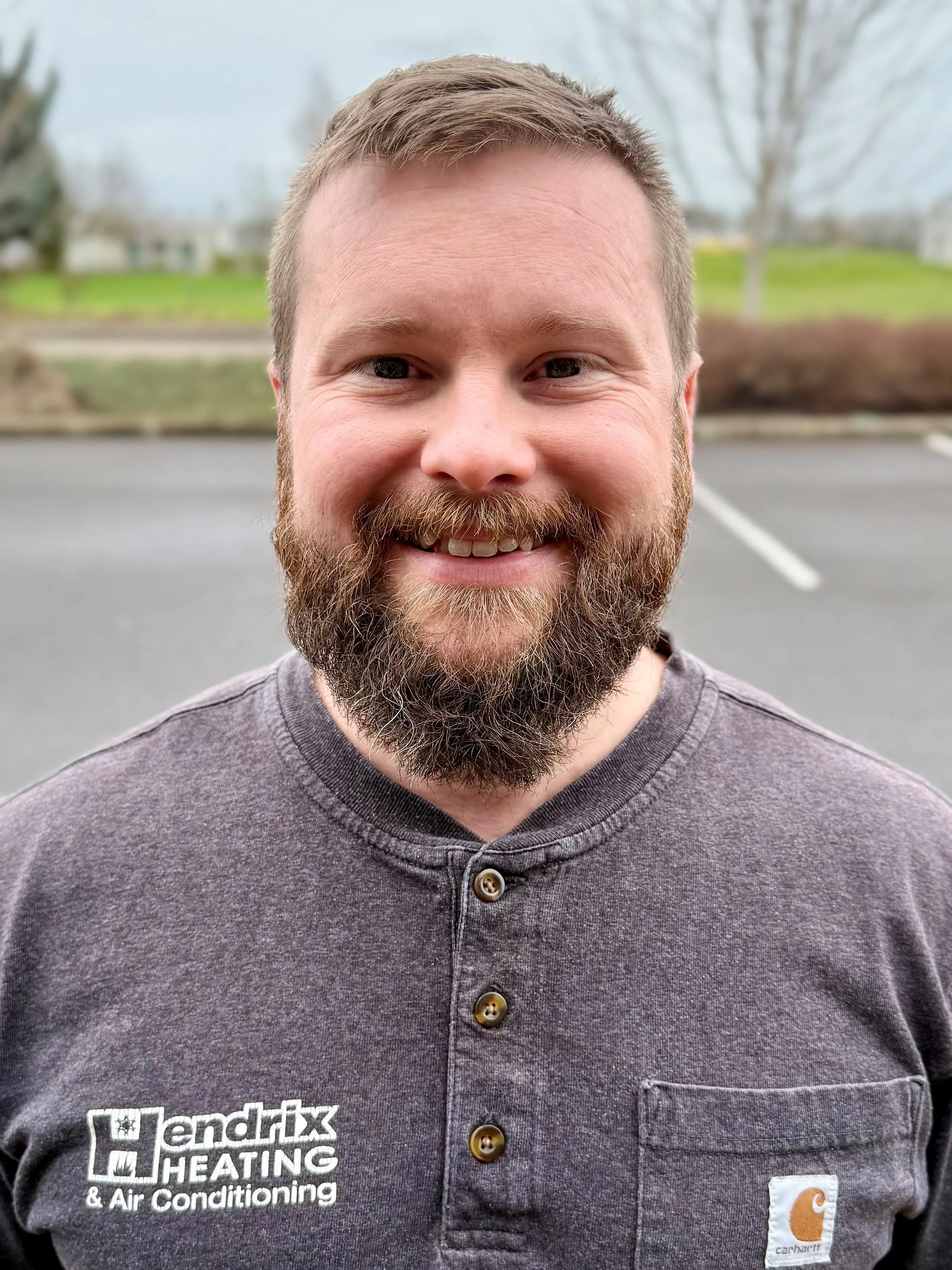 Man wearing a Hendrix Heating & Air Conditioning shirt standing outside with trees in the background.