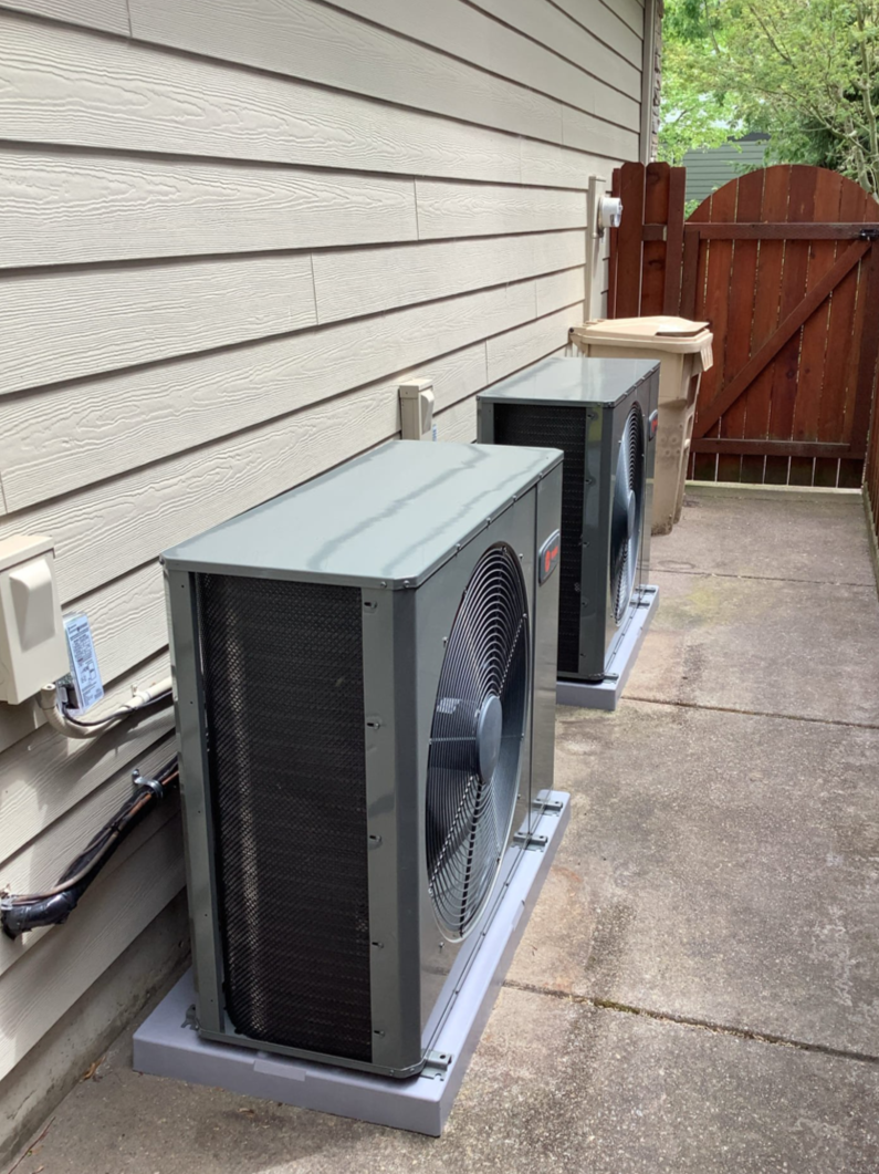 After photo showing two new side-discharge outdoor AC units installed in a narrow side yard with improved clearance and access.