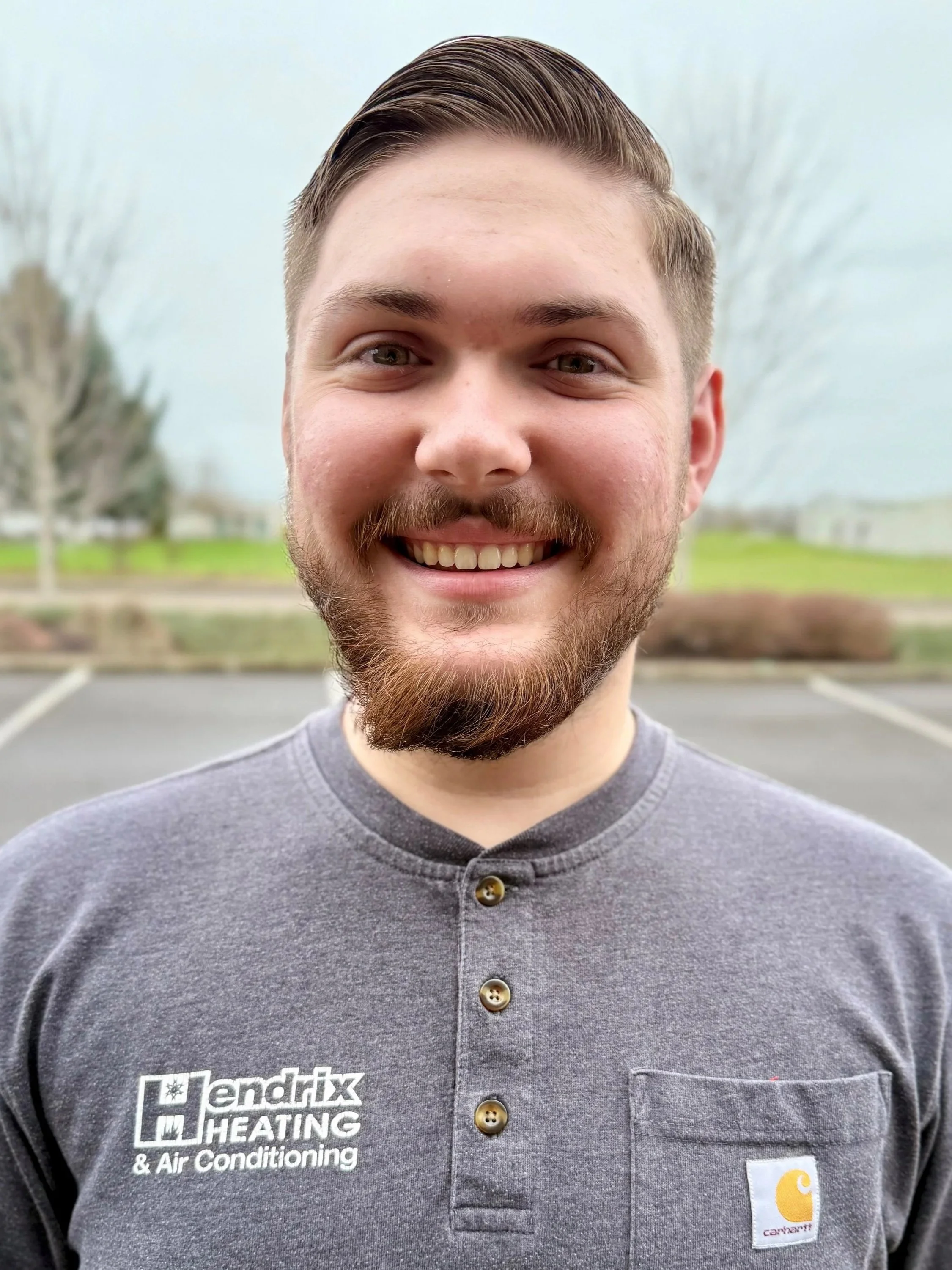 Person wearing a hoodie and cap, standing outdoors with trees in the background.