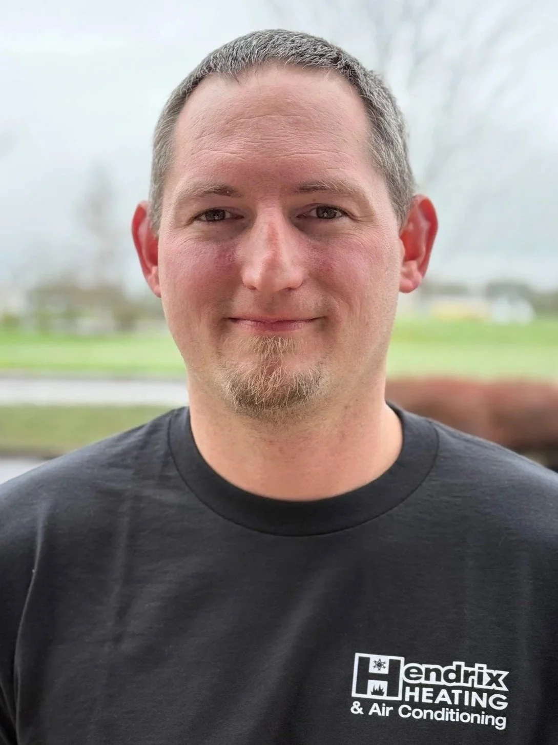 Man in a hoodie standing outdoors with trees in the background.